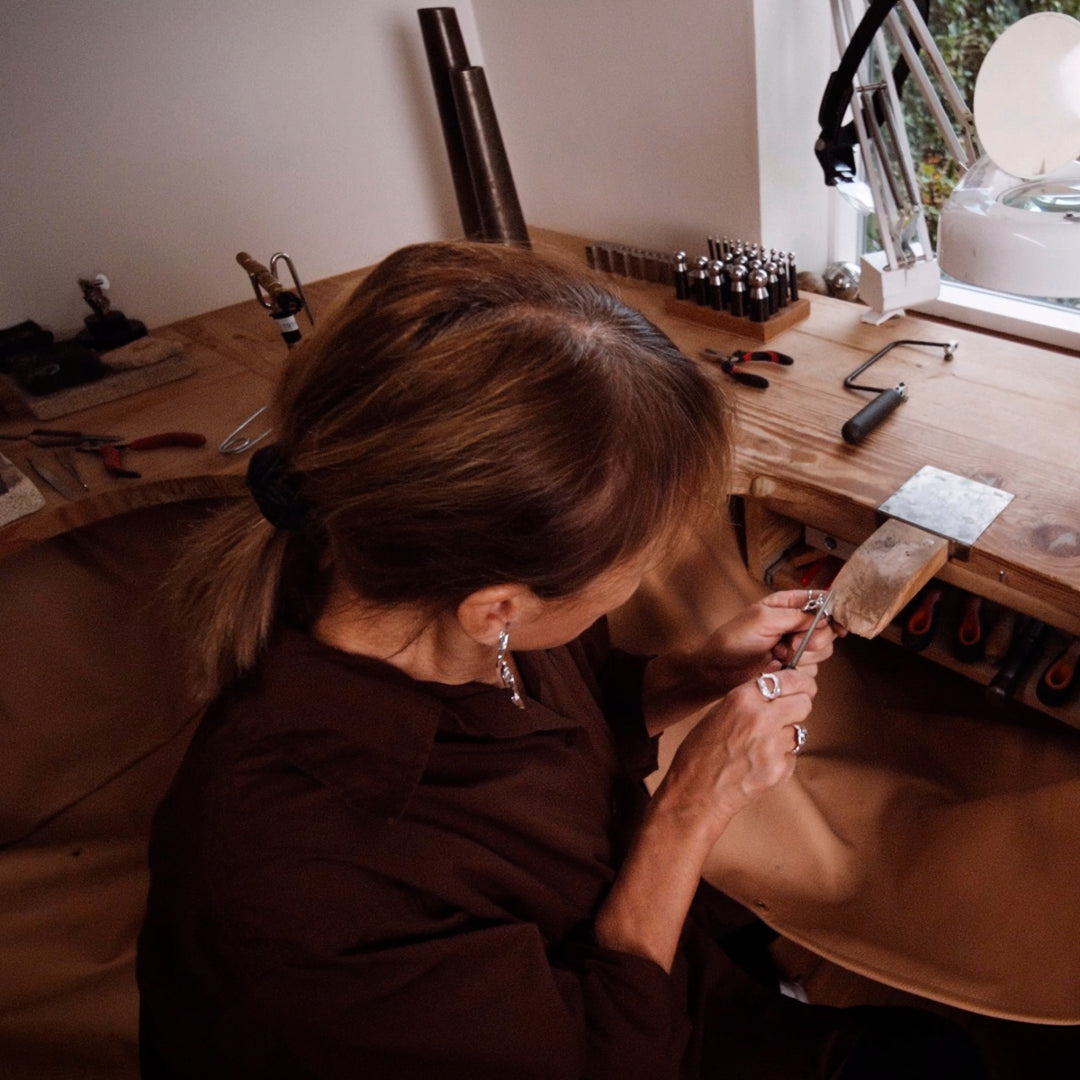 A woman crafting a piece of wood indoors, surrounded by tools, reflecting craftsmanship and creativity.