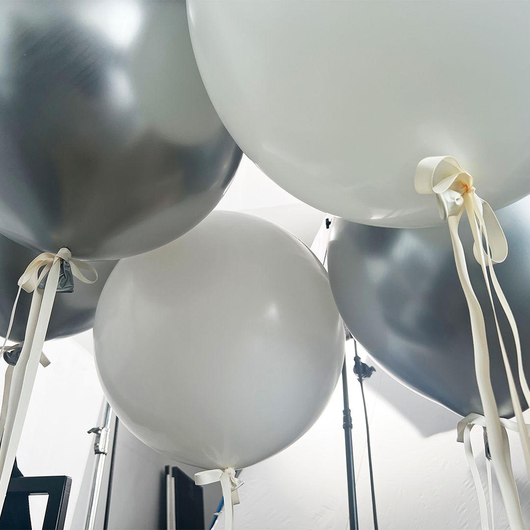 A group of white balloons with ribbons, highlighting a central balloon adorned with a bow, suggesting a celebratory atmosphere.