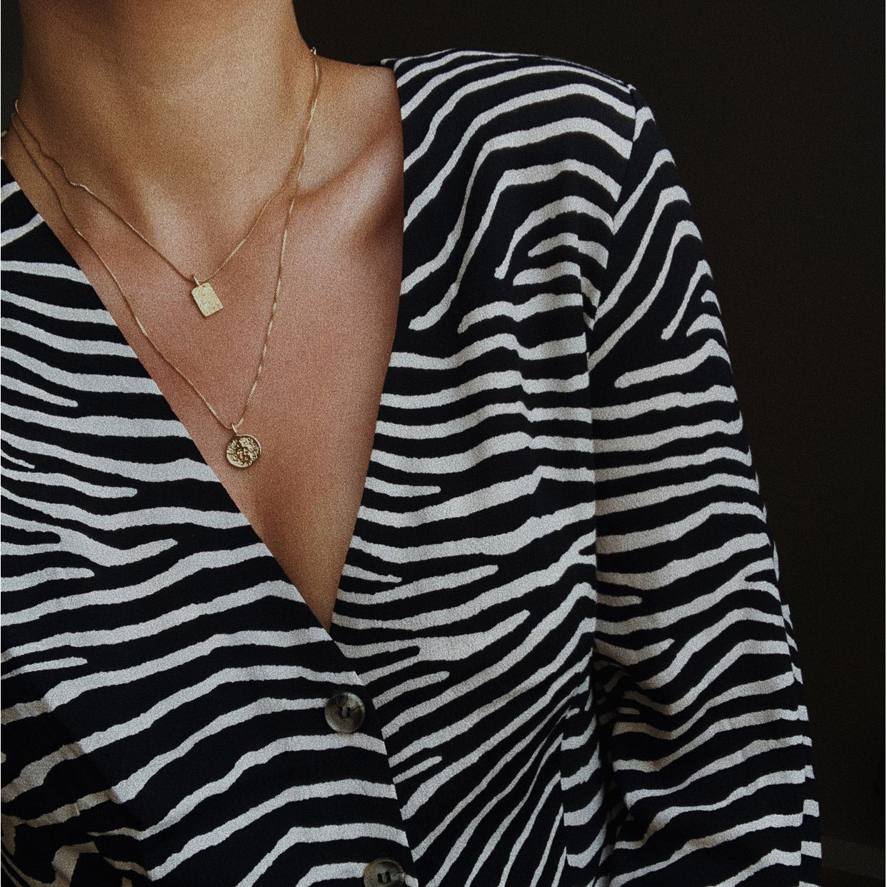 Woman wearing a zebra print shirt, showcasing the VALKYRIA coin necklace 2-in-1 set, featuring gold-plated chains with rustic Norse mythology-inspired serpent and raven motifs.