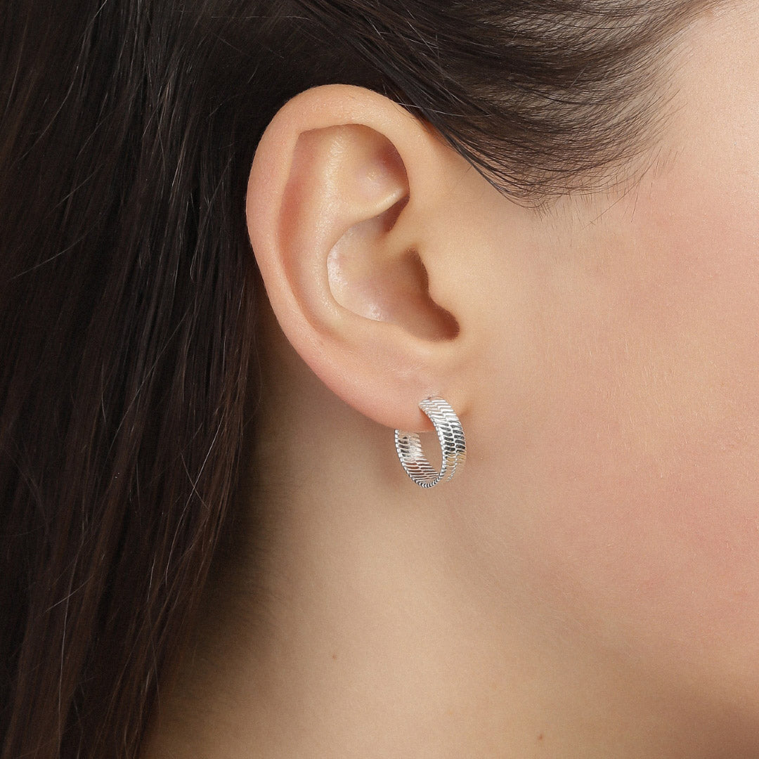 Close-up of a woman's ear wearing YGGDRASIL earrings silver-plated, showcasing embossed Nordic leaf patterns on wide hoops, inspired by mythological Scandinavian design.