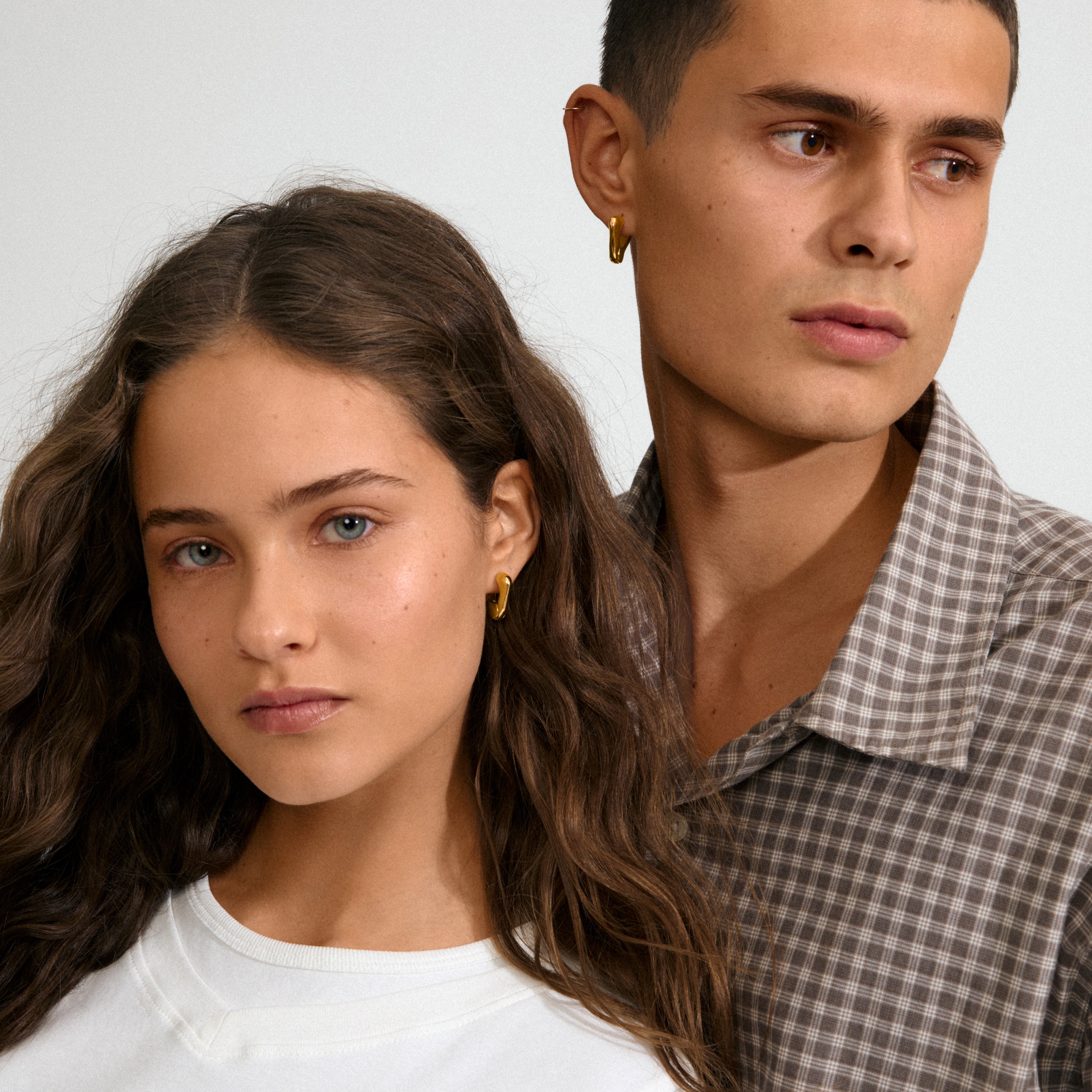 Two young adults showcase Pilgrim's FREE gold-plated hoop earrings, blending sculptural elegance and minimalist style, reflecting the brand's commitment to trendy, sustainable fashion.