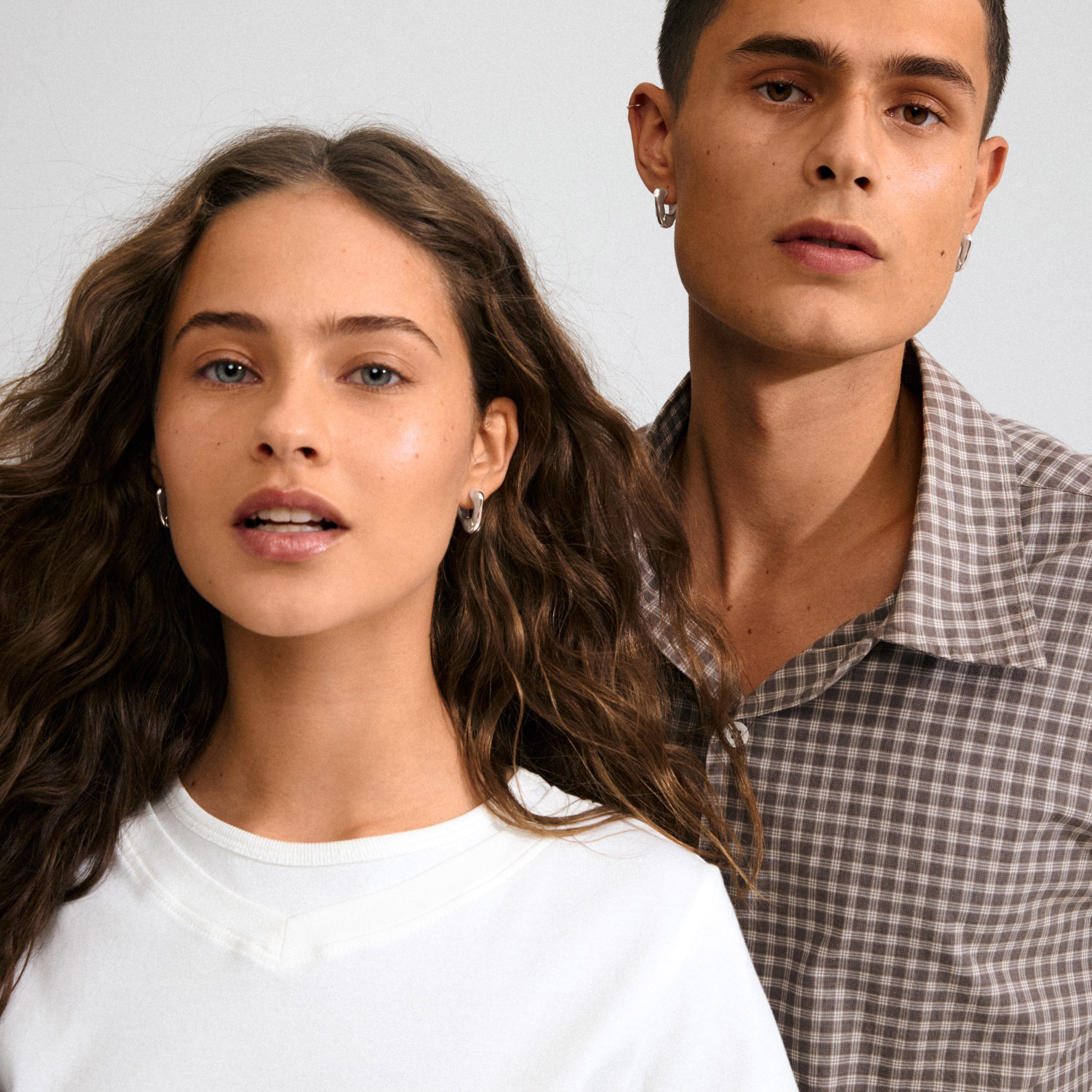 Two young adults showcasing Pilgrim's FREE earrings, silver-plated with a sculptural design, worn by the woman, embodying modern elegance and sustainable craftsmanship.