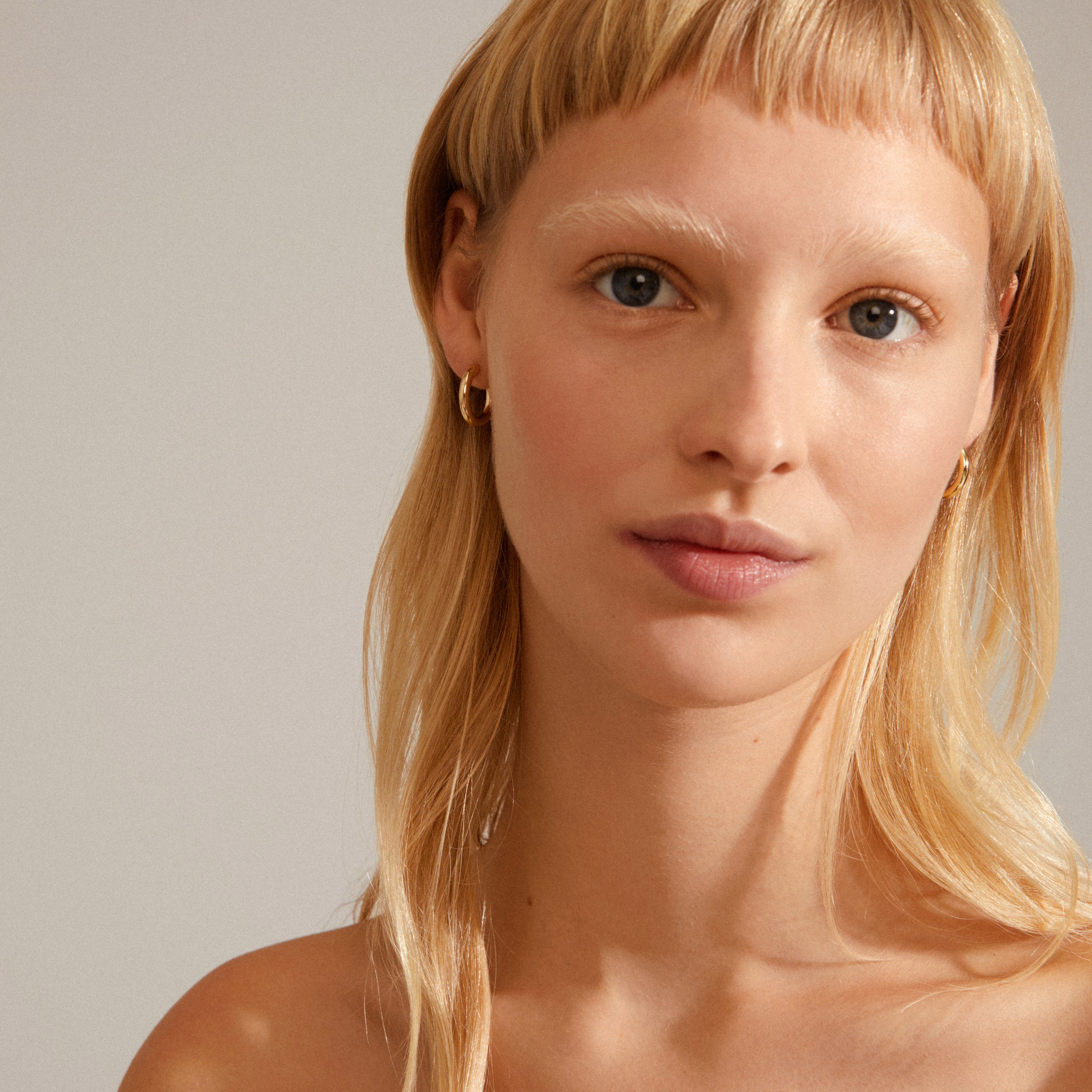 Close-up of a woman wearing DOLAG gold-plated chunky hoop earrings, showcasing their smooth, shiny surface, embodying Pilgrim's blend of trend and timeless style.
