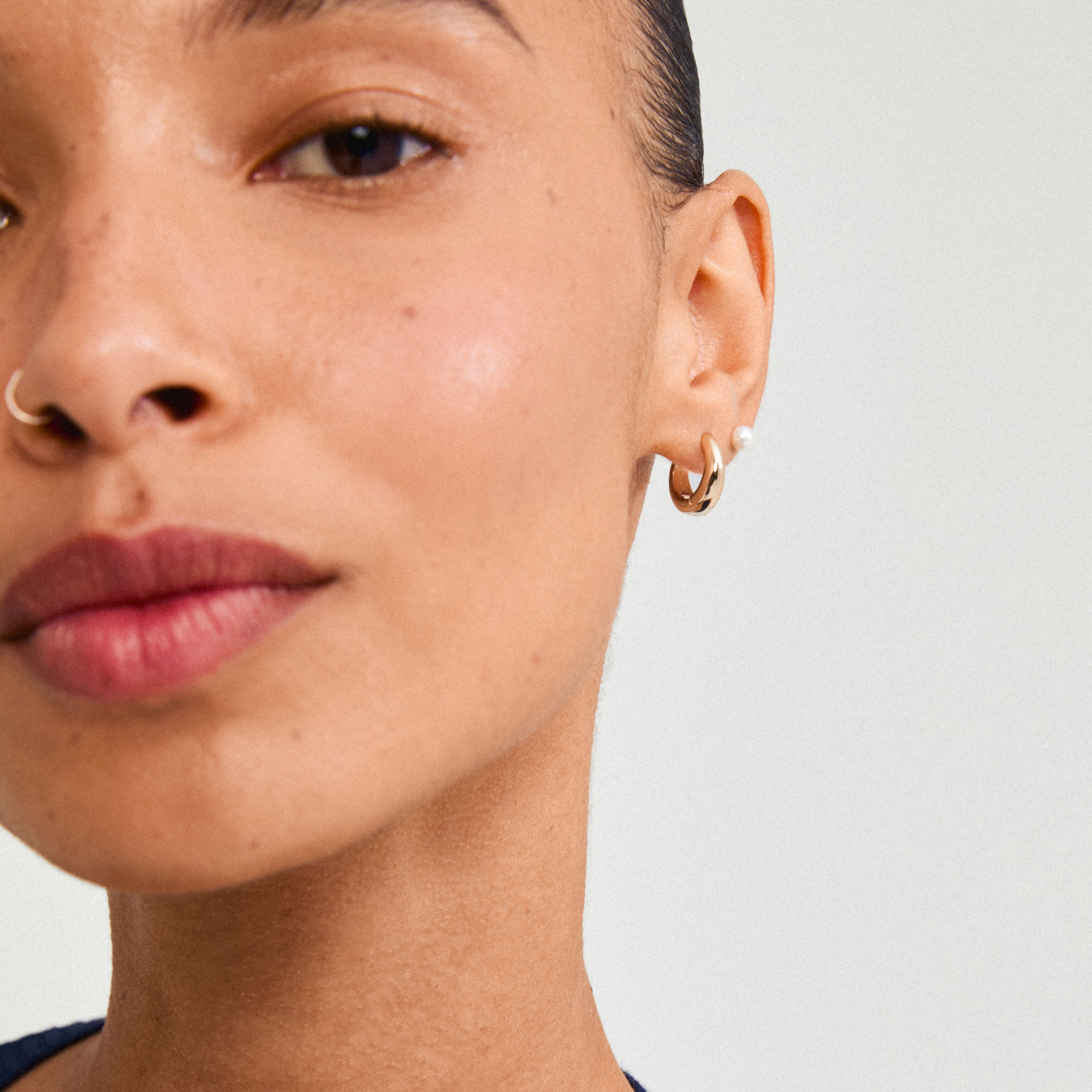 Close-up of a woman's ear wearing Pilgrim's STARLIGHT earrings, showcasing a gold-plated huggie hoop and a freshwater pearl stud.