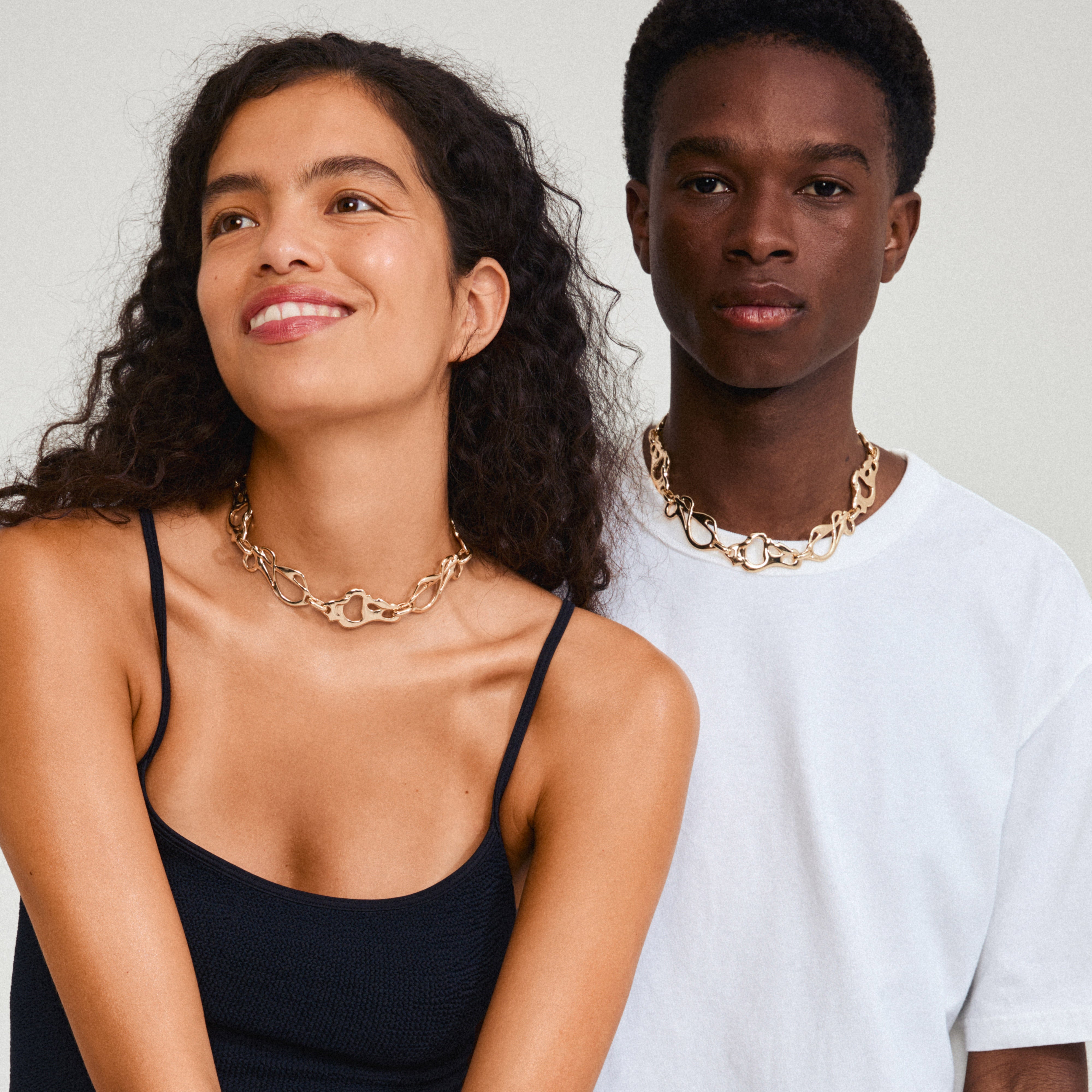 STARRLIGHT necklace gold-plated worn by a smiling woman, showcasing interconnected abstract links. A stylish statement piece inspired by nature's fluid forms.