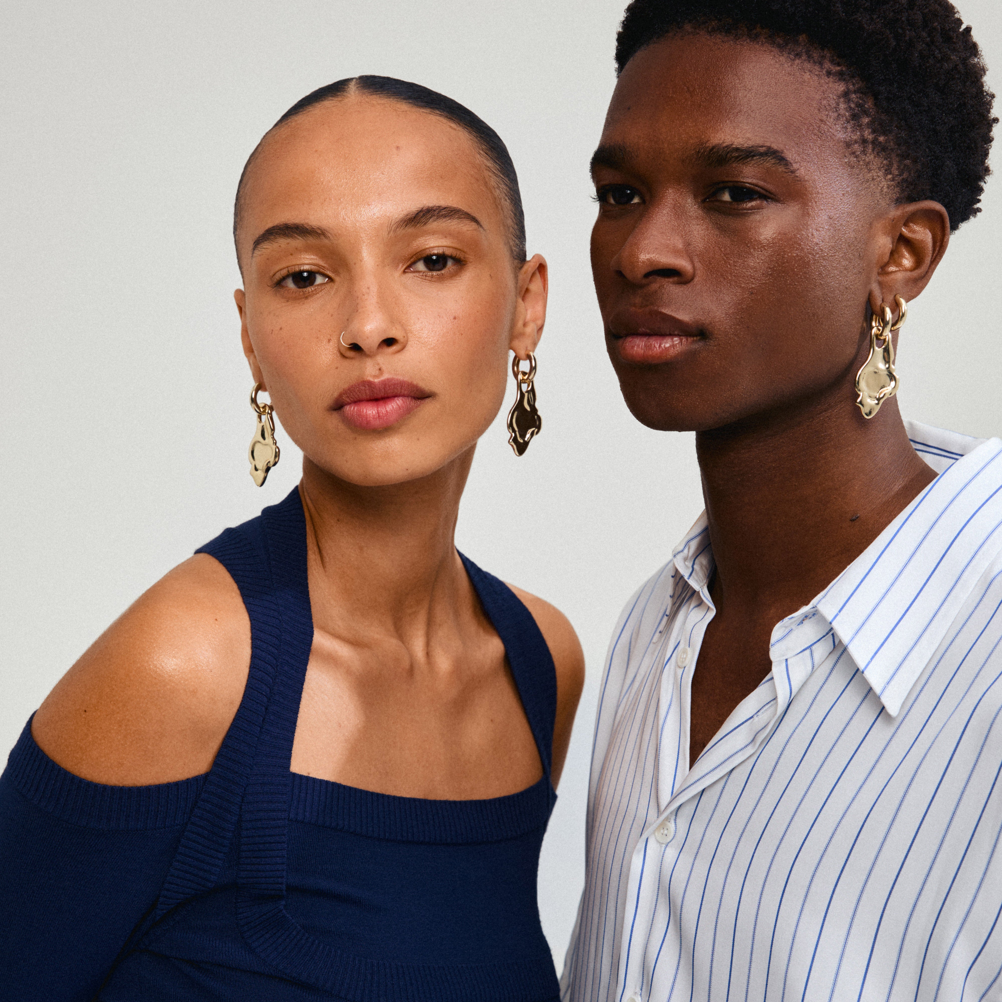 A man and woman model Pilgrim's STARLIGHT earrings, showcasing the gold-plated chunky hoops with organic pendants for a unique statement look.