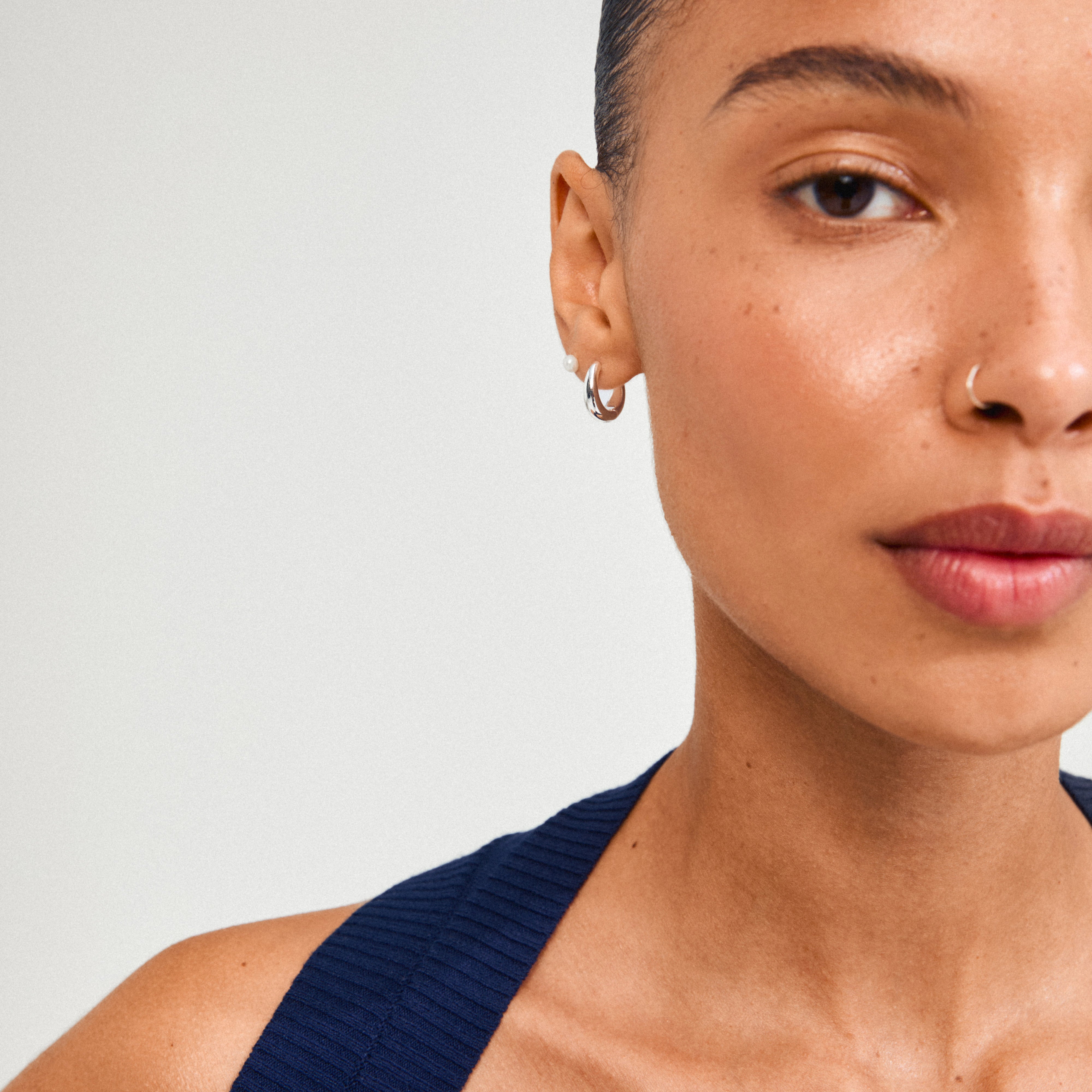 Close-up of a woman wearing Pilgrim's STARLIGHT earrings, featuring silver-plated freshwater pearl studs and chunky huggie hoops, highlighting minimalist design and sustainable style.