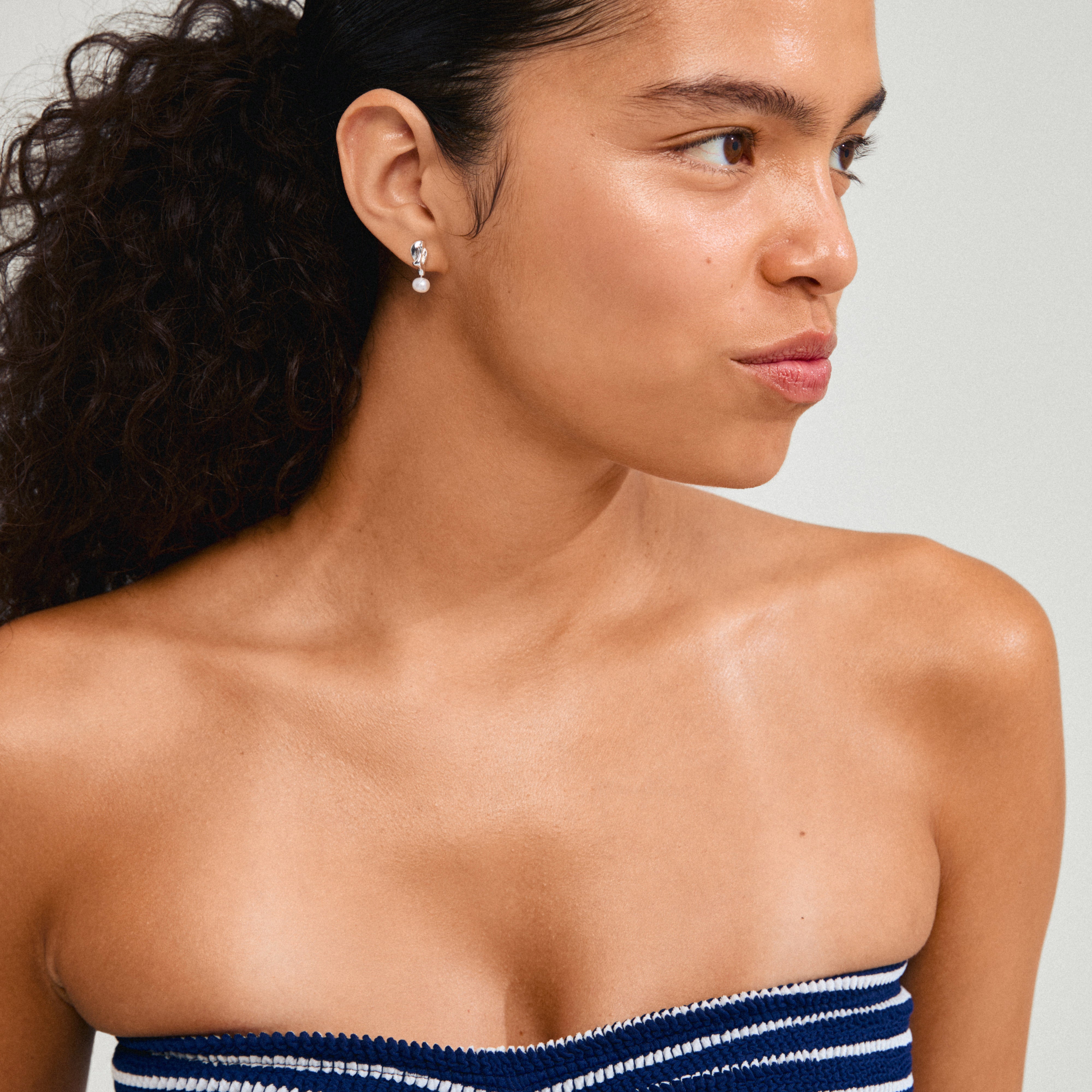 Woman wearing Pilgrim's STARLIGHT silver-plated pearl earrings, showcasing their organic shape and genuine freshwater pearl pendants, inspired by the sea.