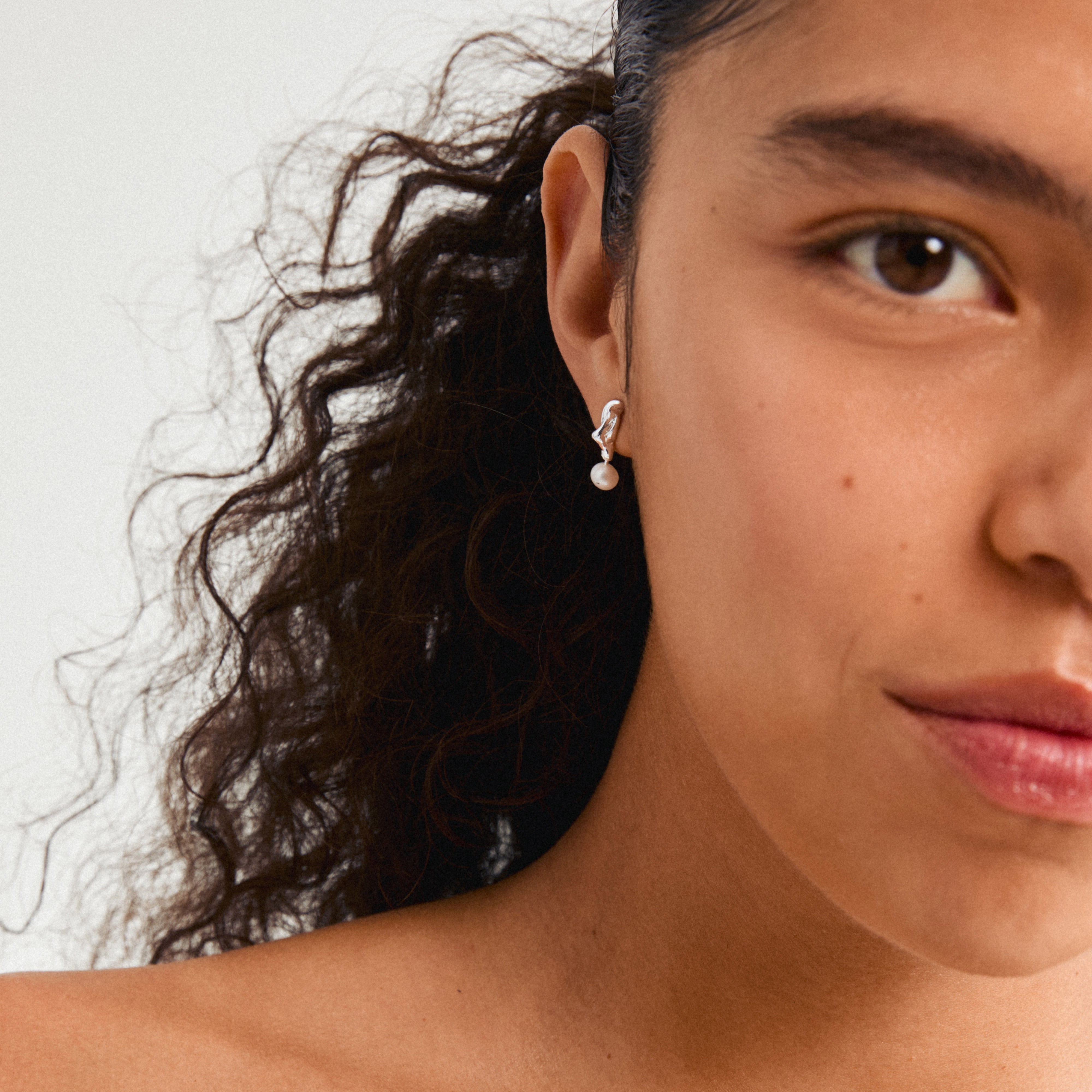 Close-up of a woman's ear adorned with Pilgrim's STARLIGHT silver-plated pearl earring, featuring a wavy design with a genuine freshwater pearl pendant.