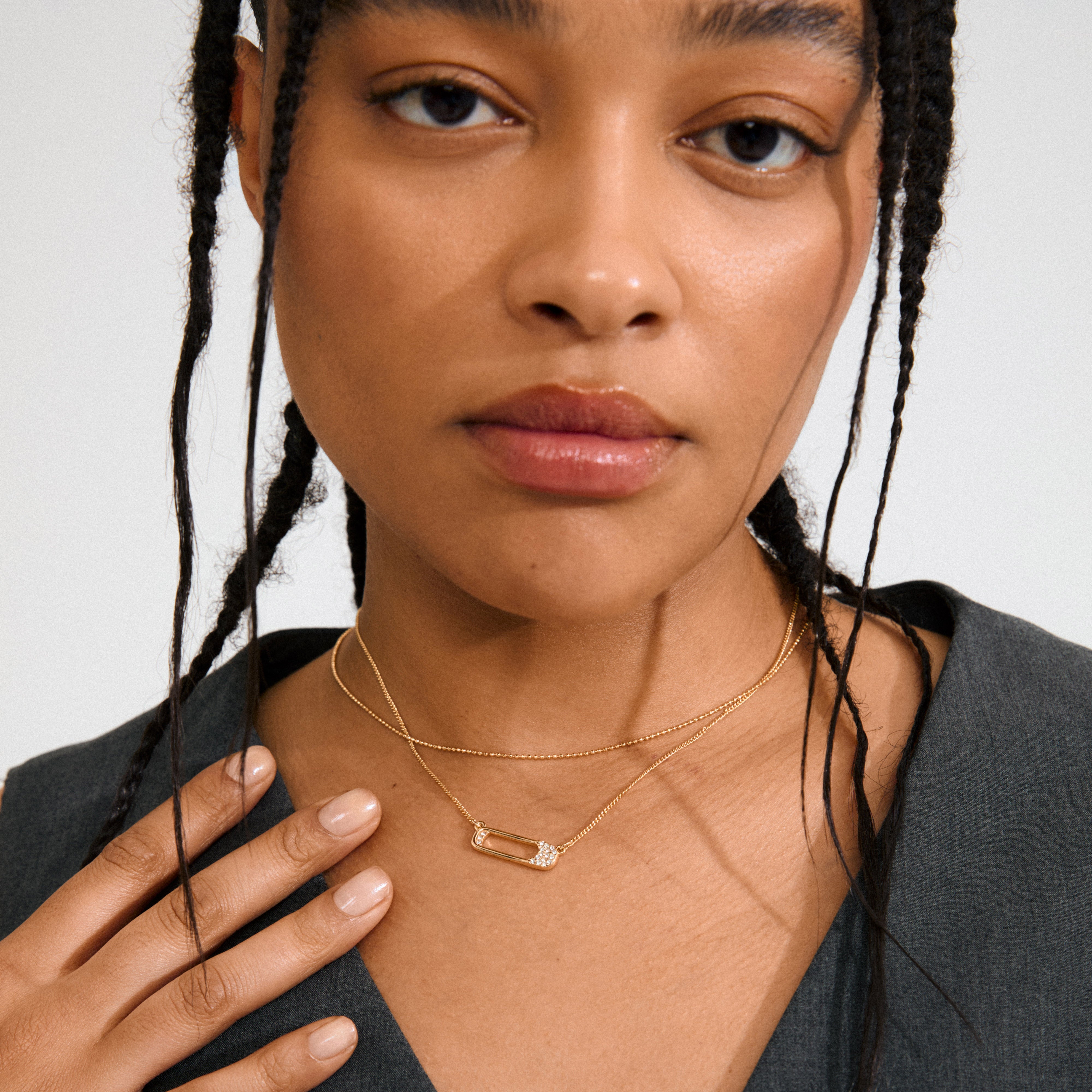 Close-up of a woman wearing the gold-plated INSTANT necklace set from Pilgrim, featuring delicate chains and a sparkling safety-pin-style pendant.