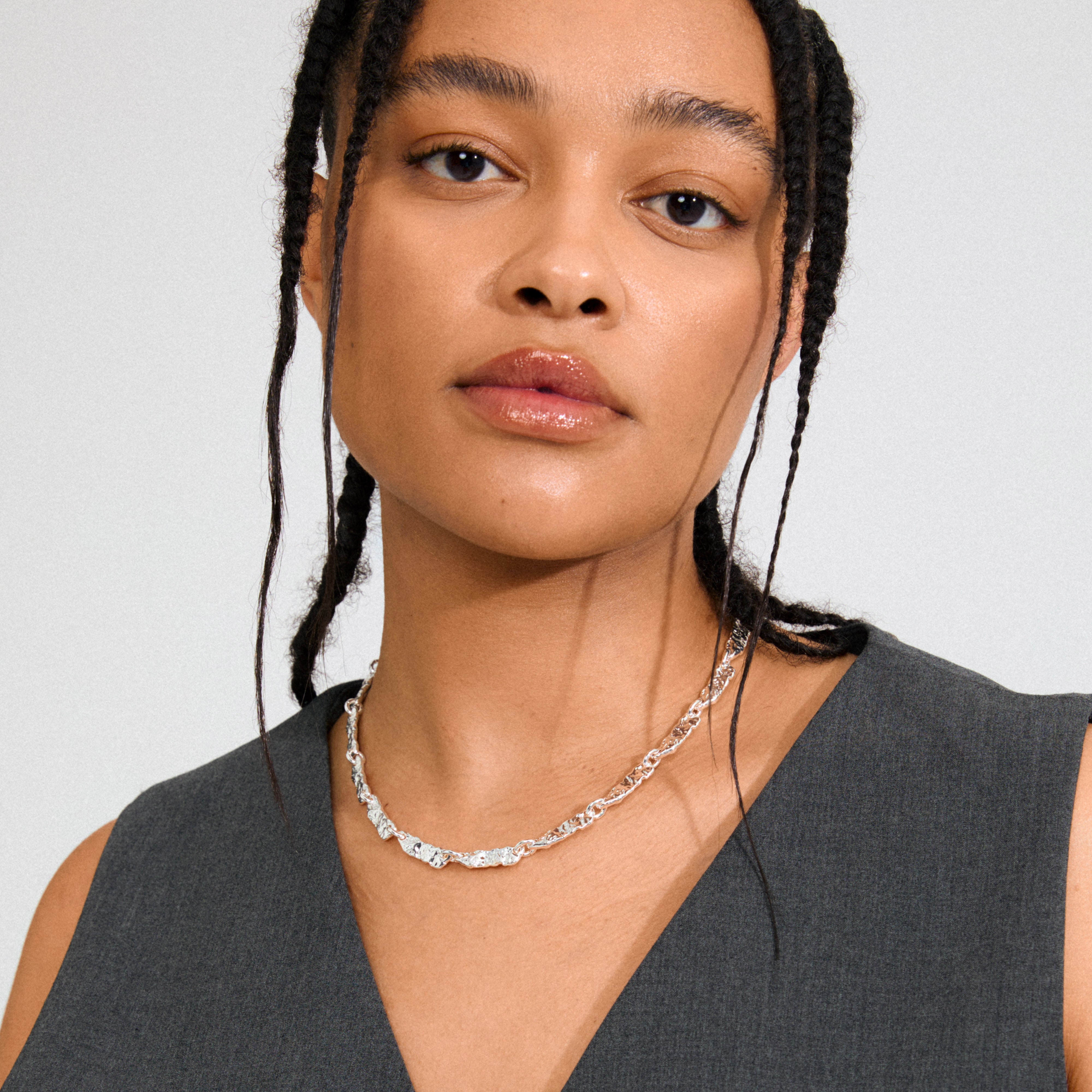 Young woman wearing Pilgrim's INSTANT necklace, silver-plated with flat, textured links, styled with her braids, showcasing a contemporary, handcrafted look.