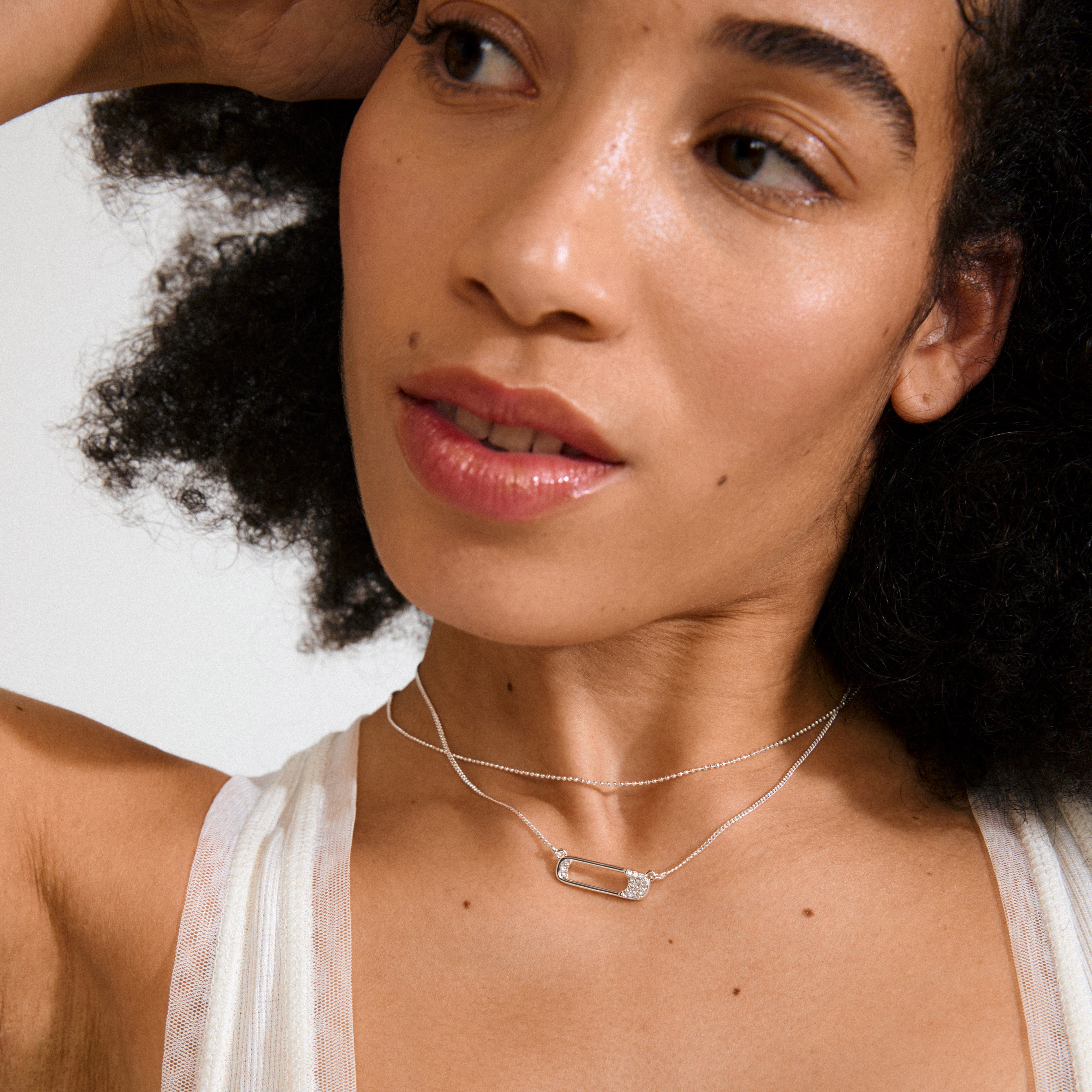 Woman wearing Pilgrim's silver-plated INSTANT necklace, featuring two layered chains with a crystal-studded safety-pin-style pendant, showcasing an edgy, stylish look.