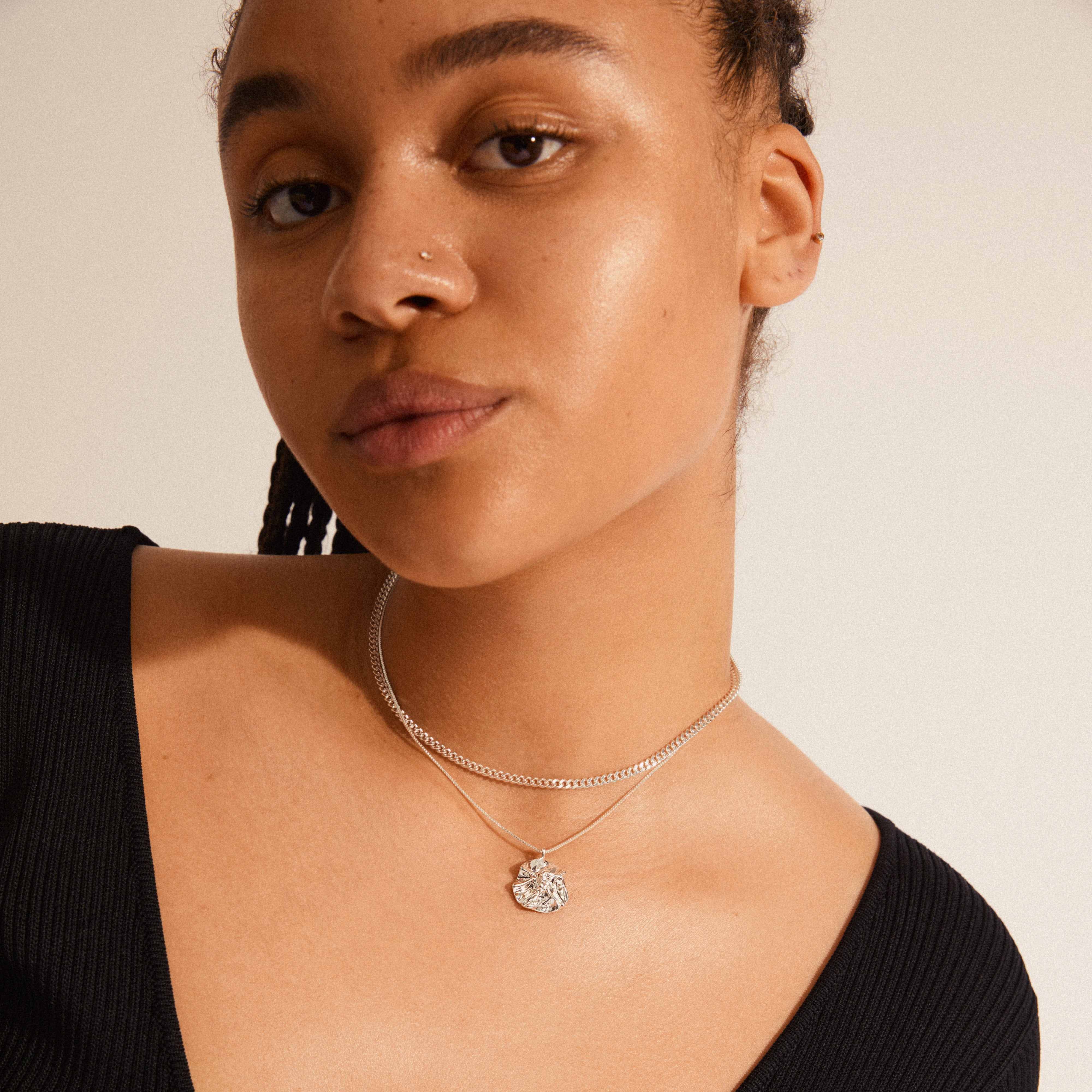 Close-up of a woman wearing Pilgrim's WILLPOWER curb & coin necklace, a 2-in-1 silver-plated set with a raw curb chain and wavy pendant.
