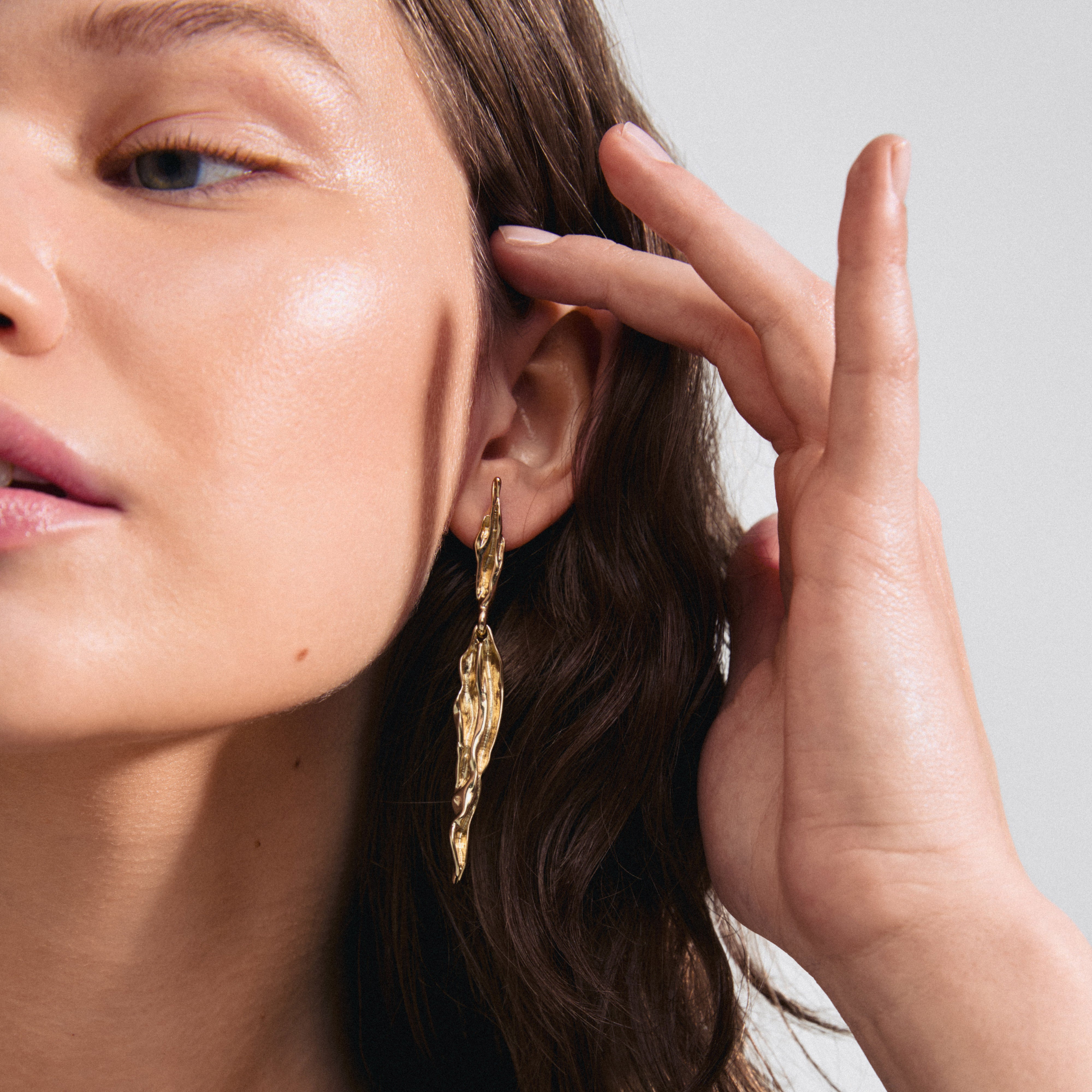 FEEL earrings gold-plated: Close-up of a woman wearing sleek, wavy gold-plated earrings, reflecting nature-inspired, organic design from Pilgrim's FEEL collection.