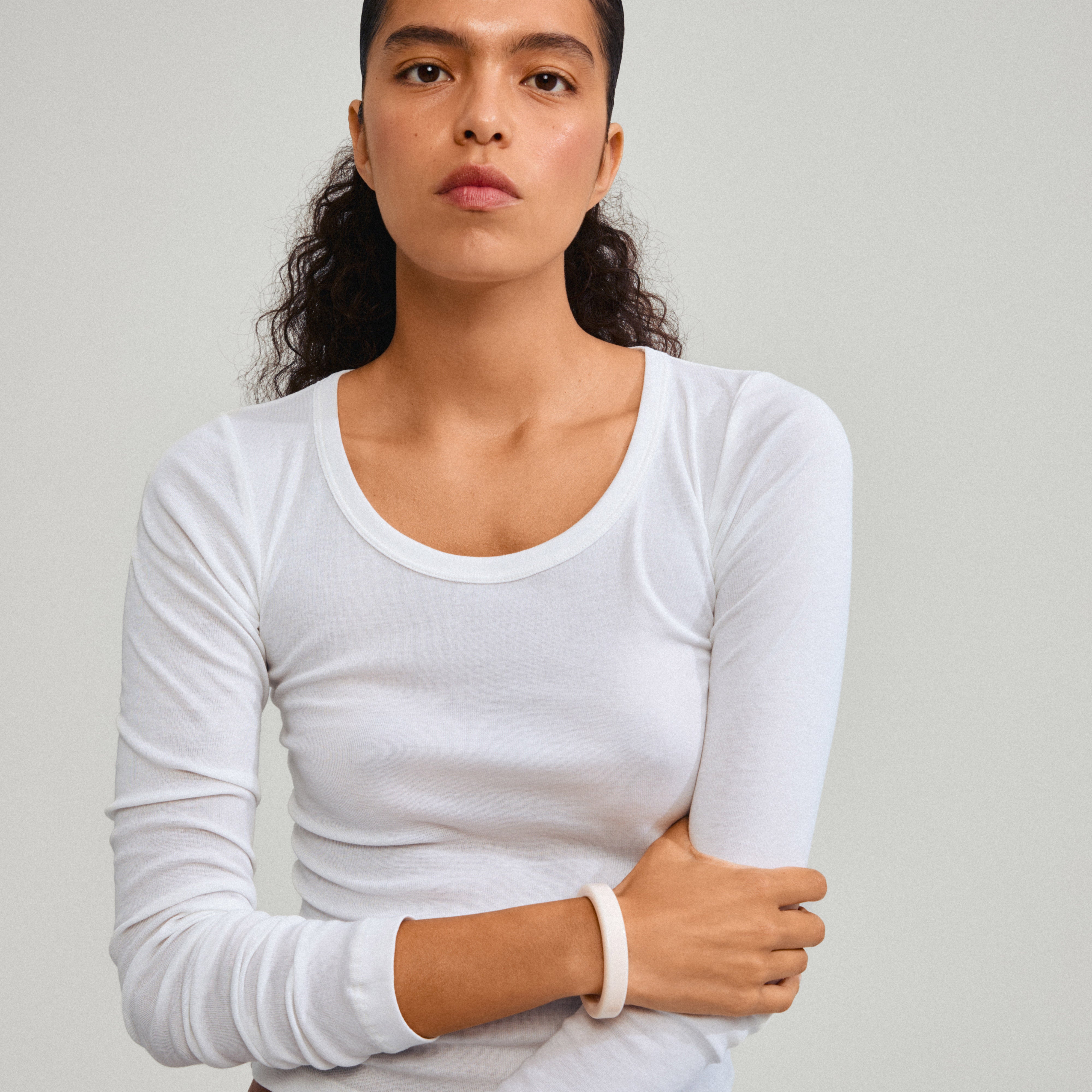 Woman wearing the ECLIPSE bangle white from Pilgrim, showcasing its simple, clean design, crafted from recycled acrylic for a chic, versatile style.