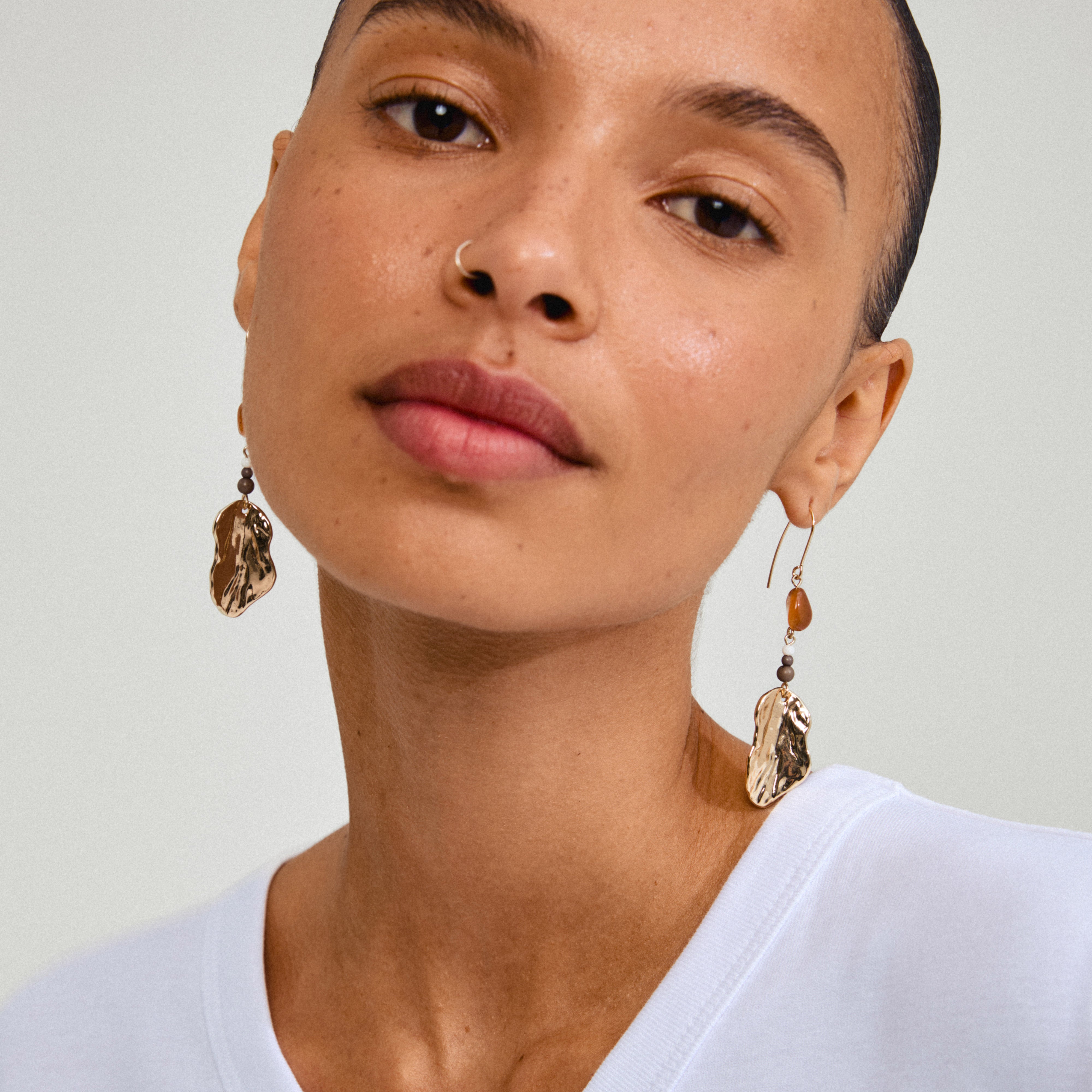 ECLIPSE earrings gold-plated featuring gold organic pendants with red Agate, worn by a woman with short hair; captures light beautifully.