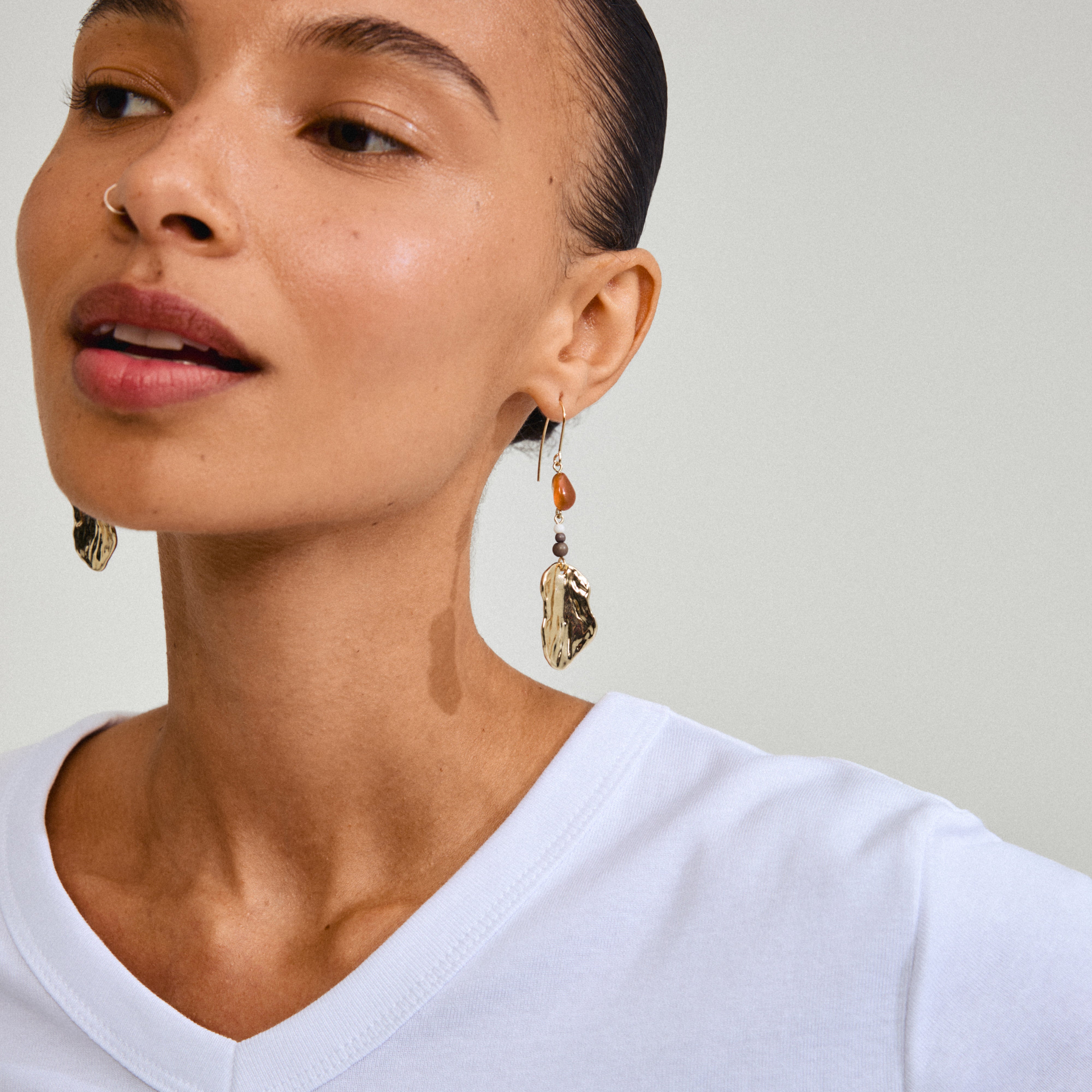 Close-up of a woman wearing Pilgrim's gold-plated ECLIPSE earrings with organic pendants and red Agate, highlighting unique bohemian style.