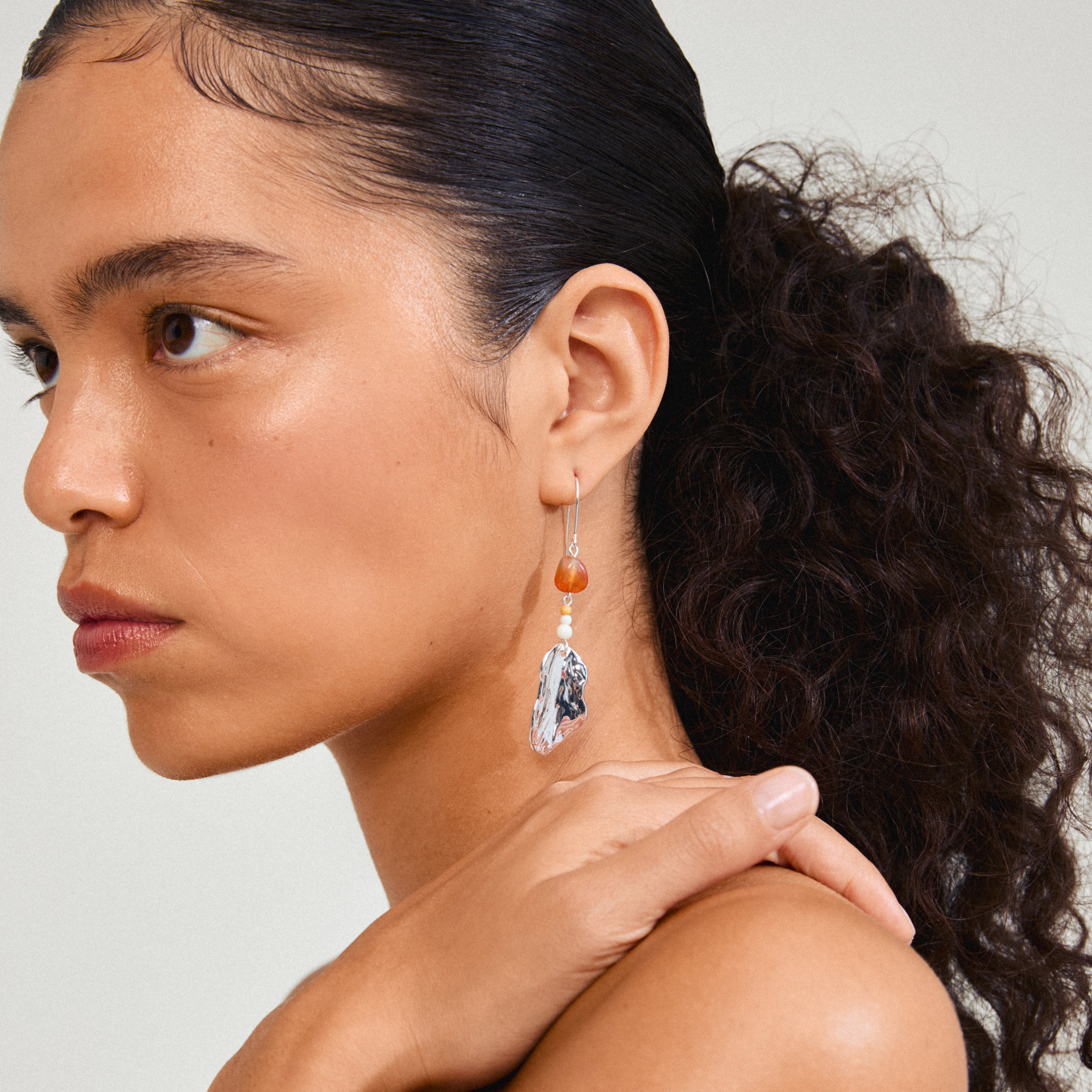 Close-up of a woman wearing Pilgrim's silver-plated ECLIPSE earrings with organic pendants and red Agate, highlighting a bohemian, nature-inspired design.