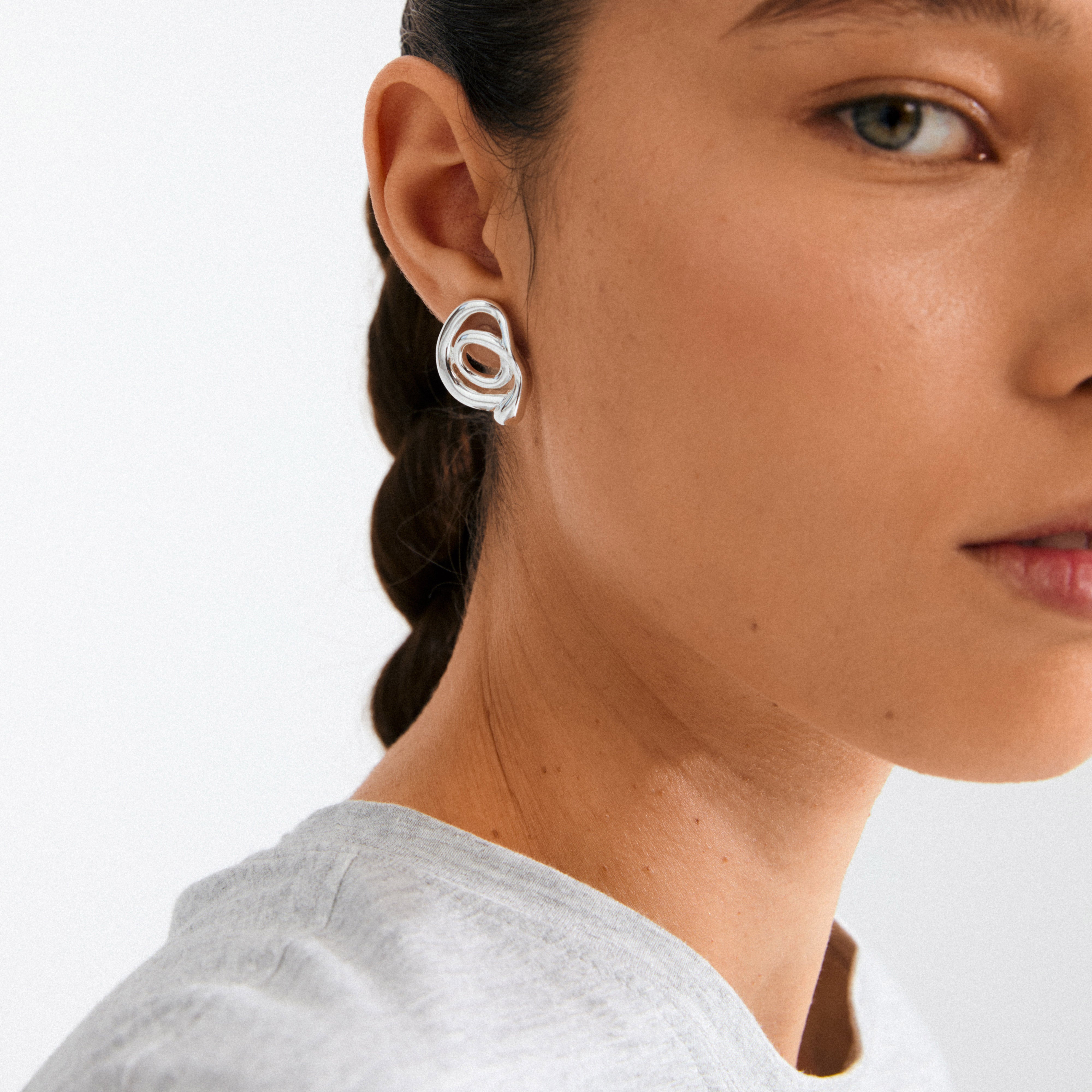 Young woman wearing a silver-plated UNFOLD earring by Pilgrim, featuring a sculptural spiral design, showcasing artistic expression and eco-friendly craftsmanship.