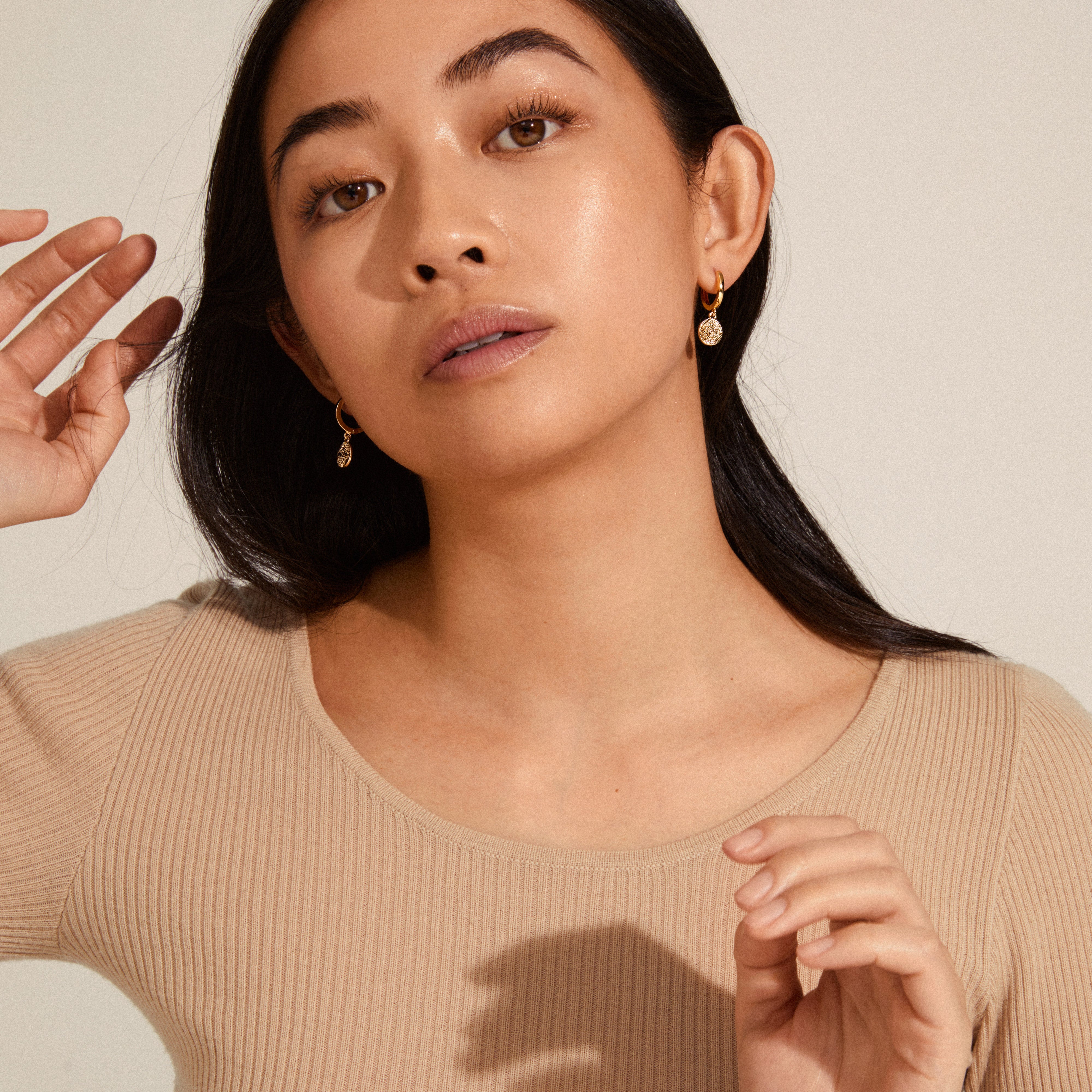 Woman wearing NOMAD coin huggie hoop earrings, gold-plated, showcasing Pilgrim's timeless, elegant design with hoop and coin pendant detail.
