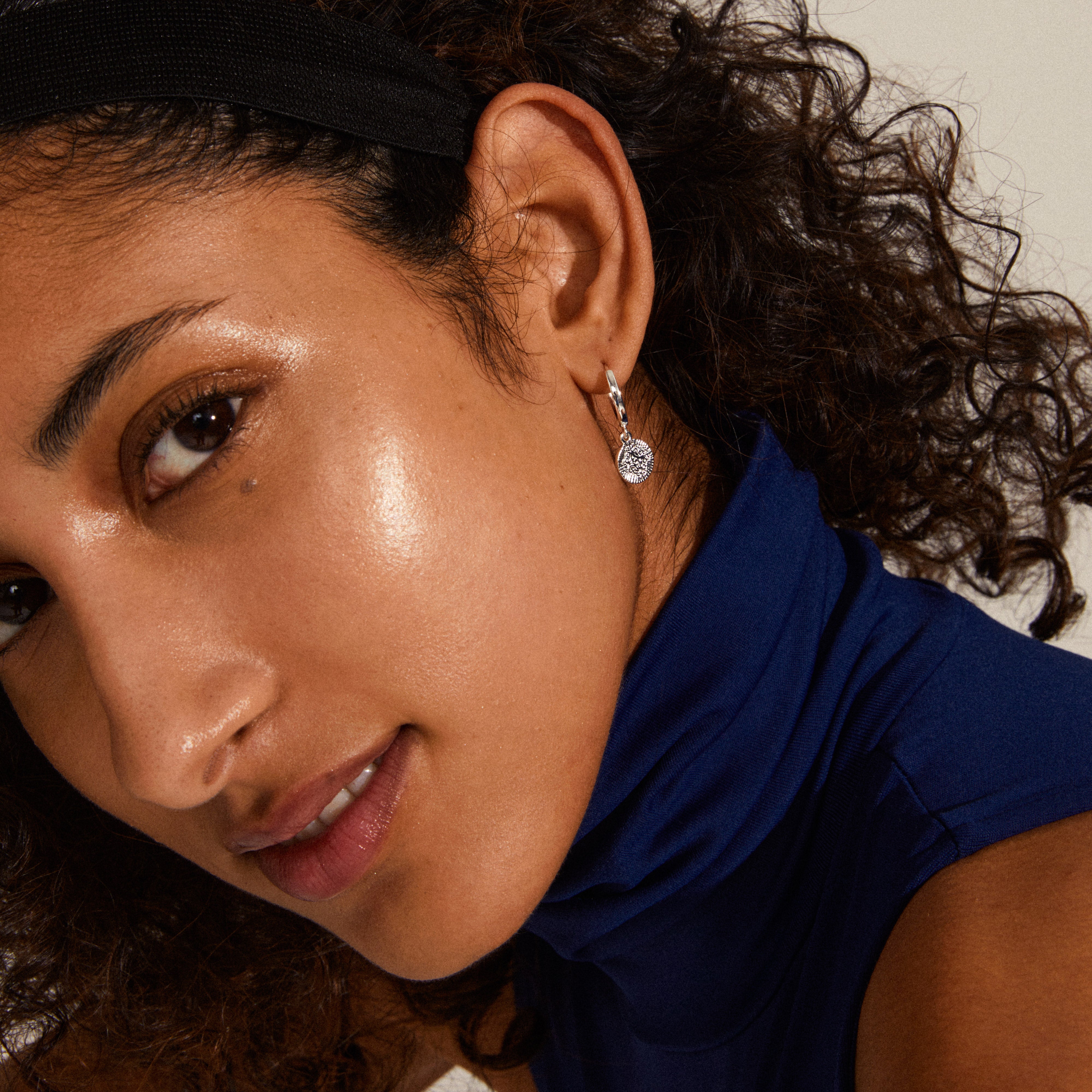 NOMAD coin huggie hoop earrings silver-plated, showcased on a woman with curly hair, highlighting the bohemian-inspired coin pendants and luxurious design.