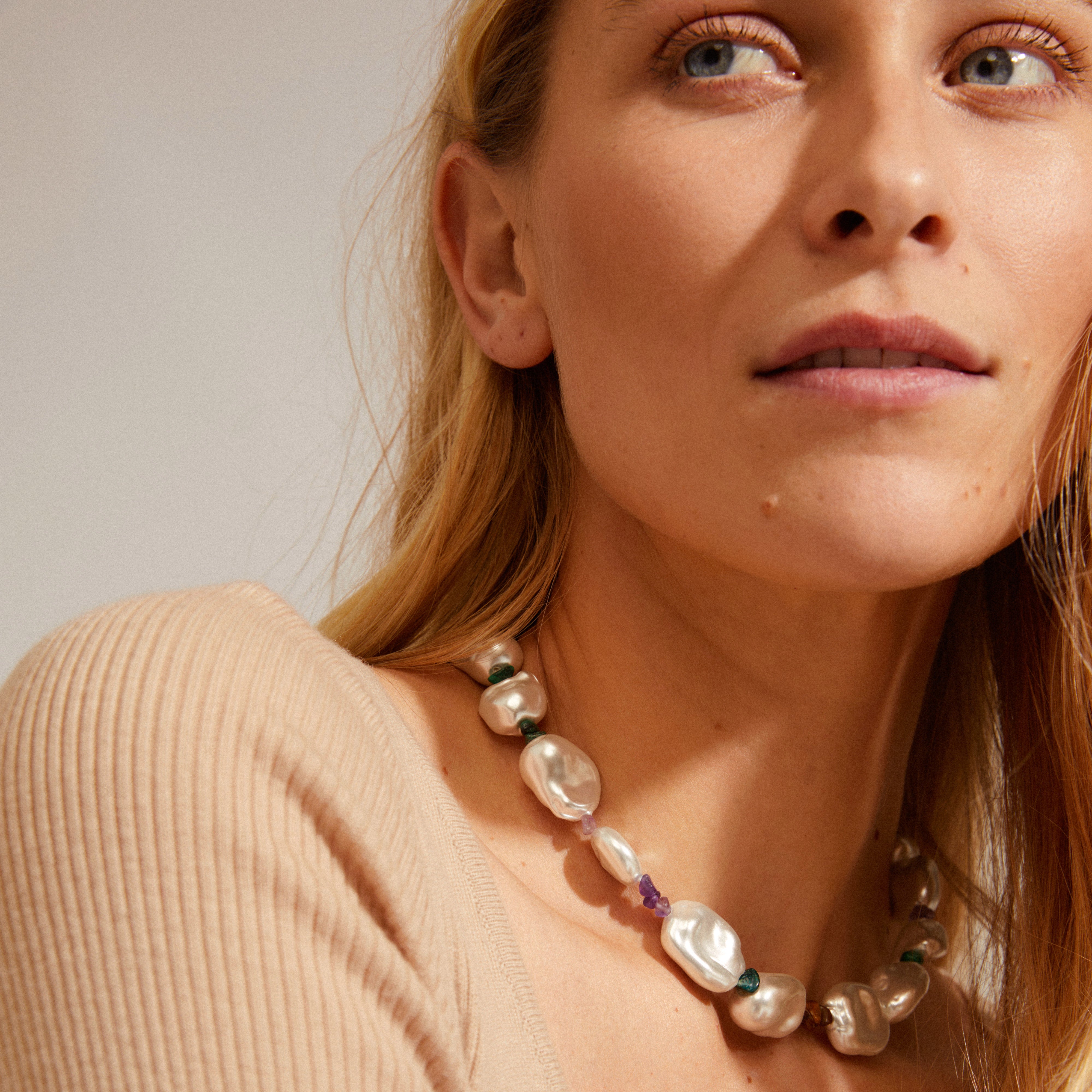 Close-up of a woman wearing Pilgrim's RHYTHM pearl necklace, featuring asymmetrical shapes with tiger's eye, malachite, and amethyst stones.
