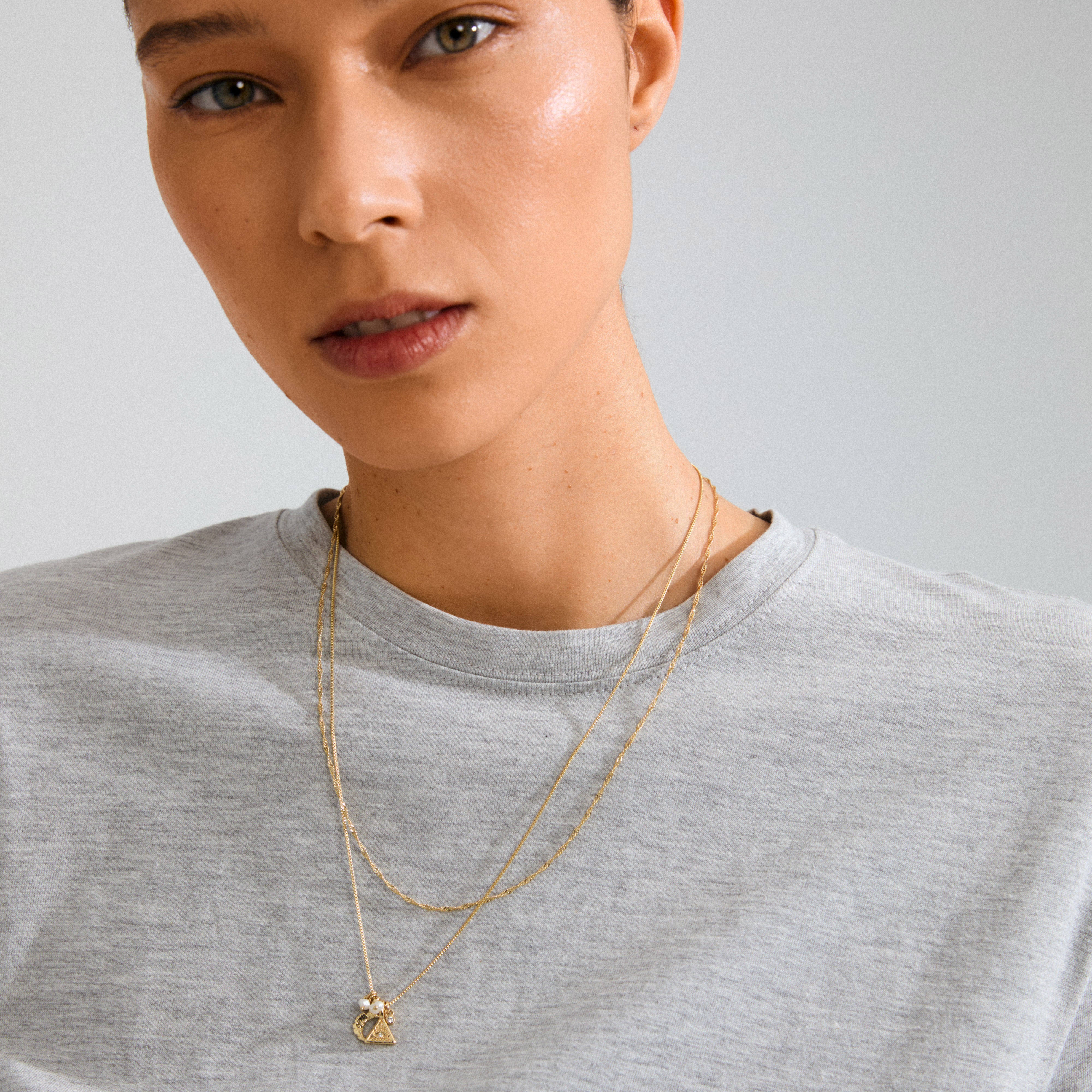 Close-up of a woman wearing Pilgrim's BETWEEN necklace 2-in-1 gold-plated, featuring a box chain, twisted chain, and spiritual pendants, embodying bohemian elegance.