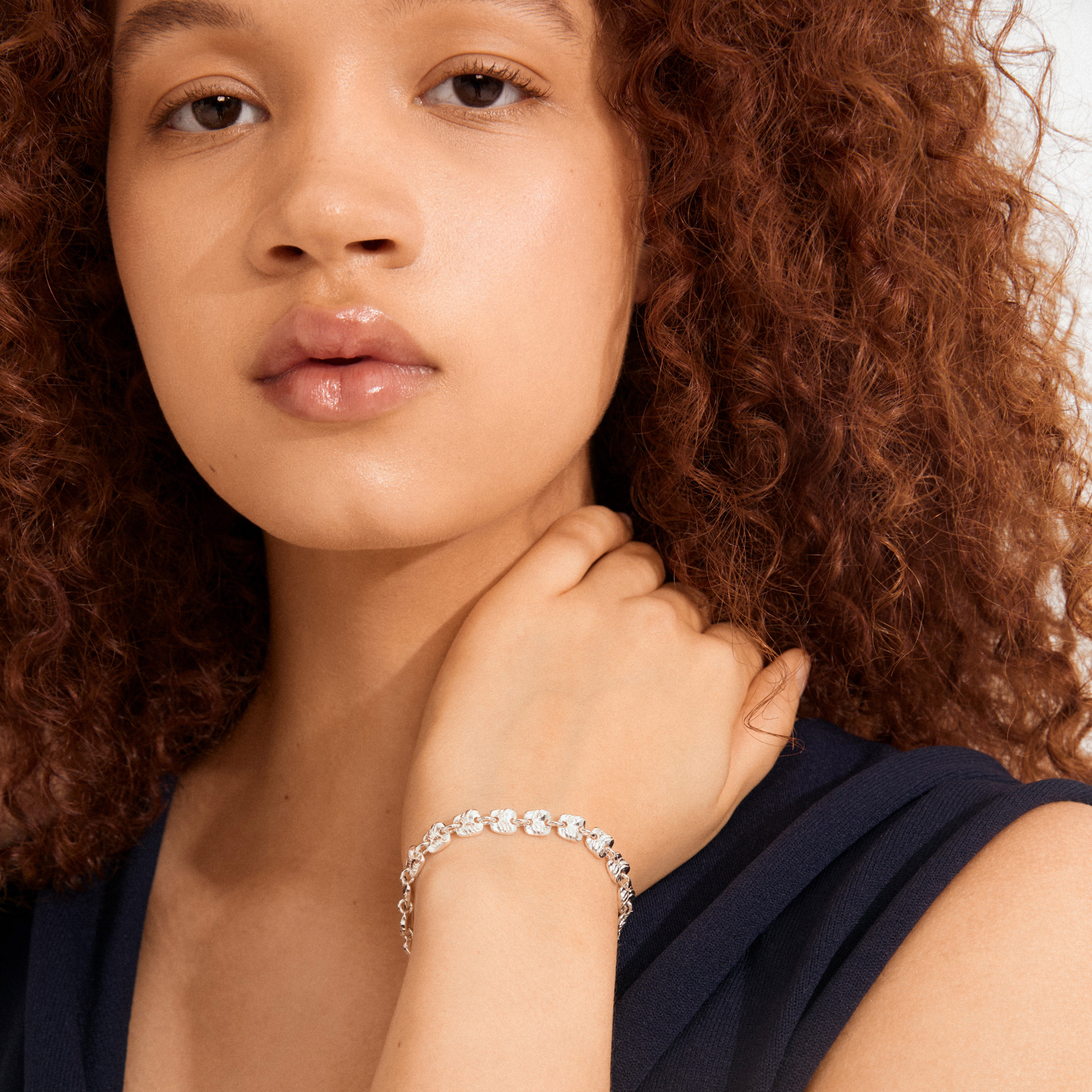 Young woman wearing Pilgrim's SENSE bracelet: a silver-plated, handcrafted piece with wavy, textured square coins, embodying minimalist elegance and Scandinavian style.