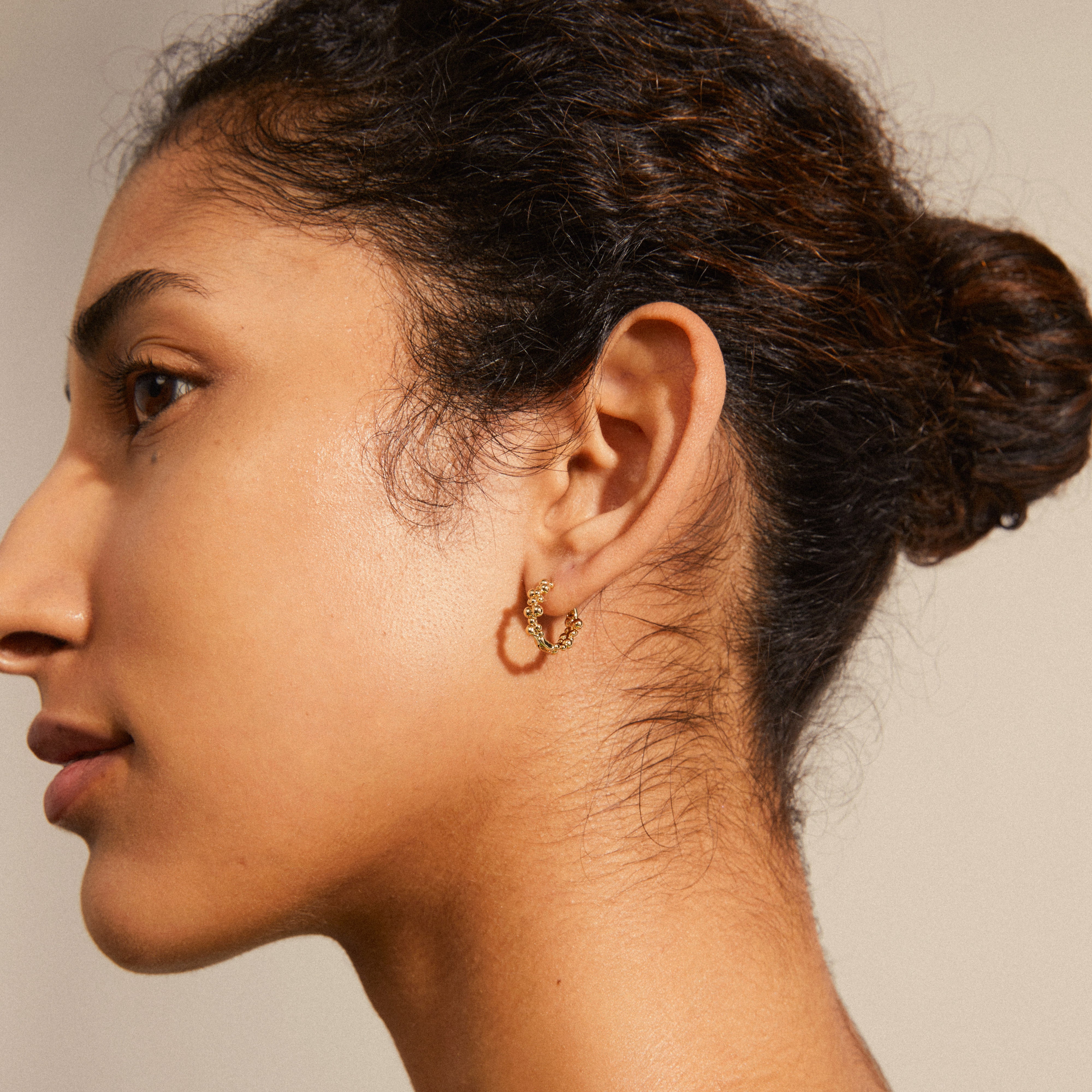 Gold-plated SOLIDARITY small bubbles hoop earrings on a woman's ear, showcasing spherical designs with a shiny finish and easy click-lock closure.