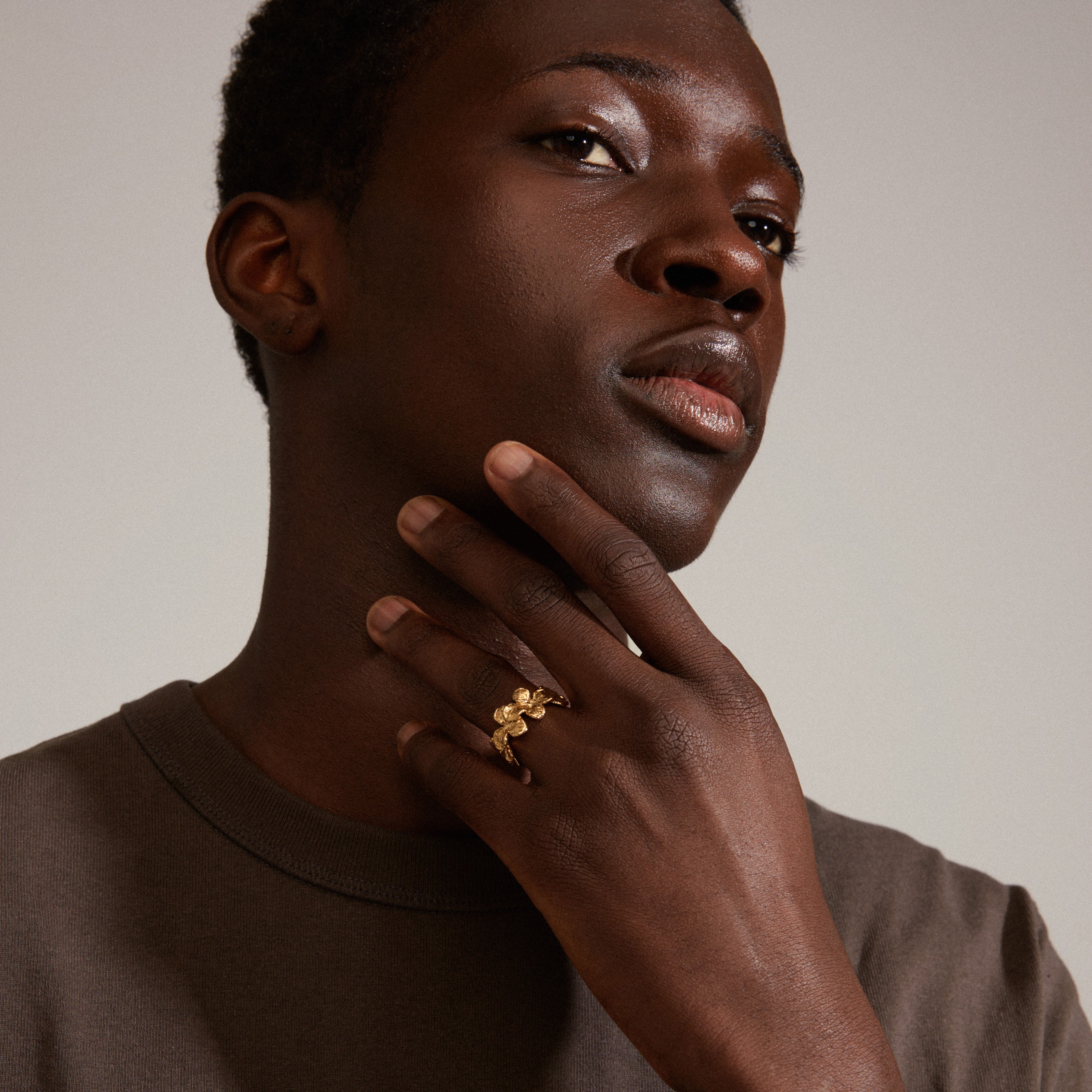 Man wearing an ECHO ring gold-plated from Pilgrim, thoughtfully posing with hand on chin. The ring features a classic flower design, embodying a handcrafted, nature-inspired style.