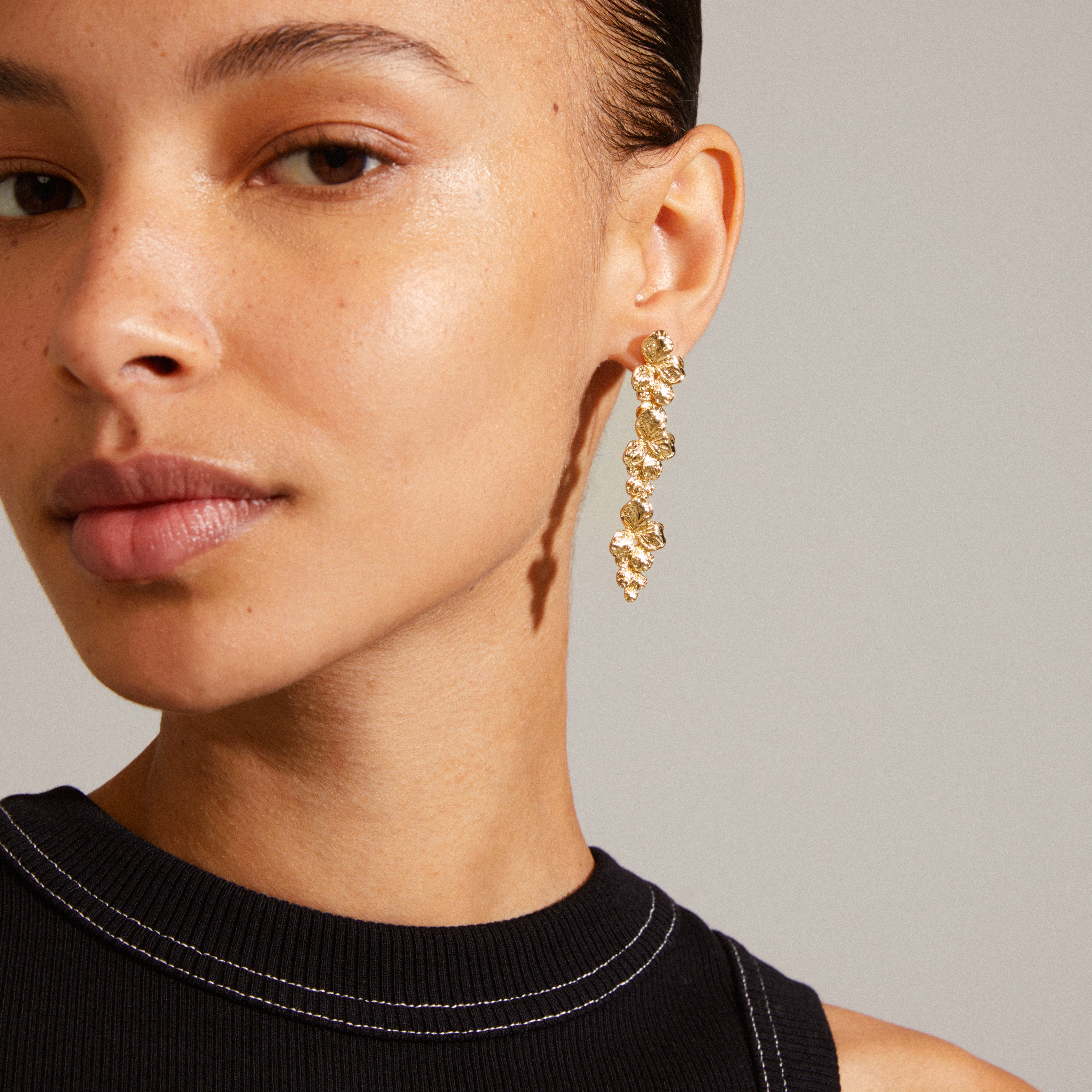 Close-up of a woman wearing Pilgrim's ECHO gold-plated earrings, featuring handcrafted flower vine design, adding elegance and shine to a party outfit.