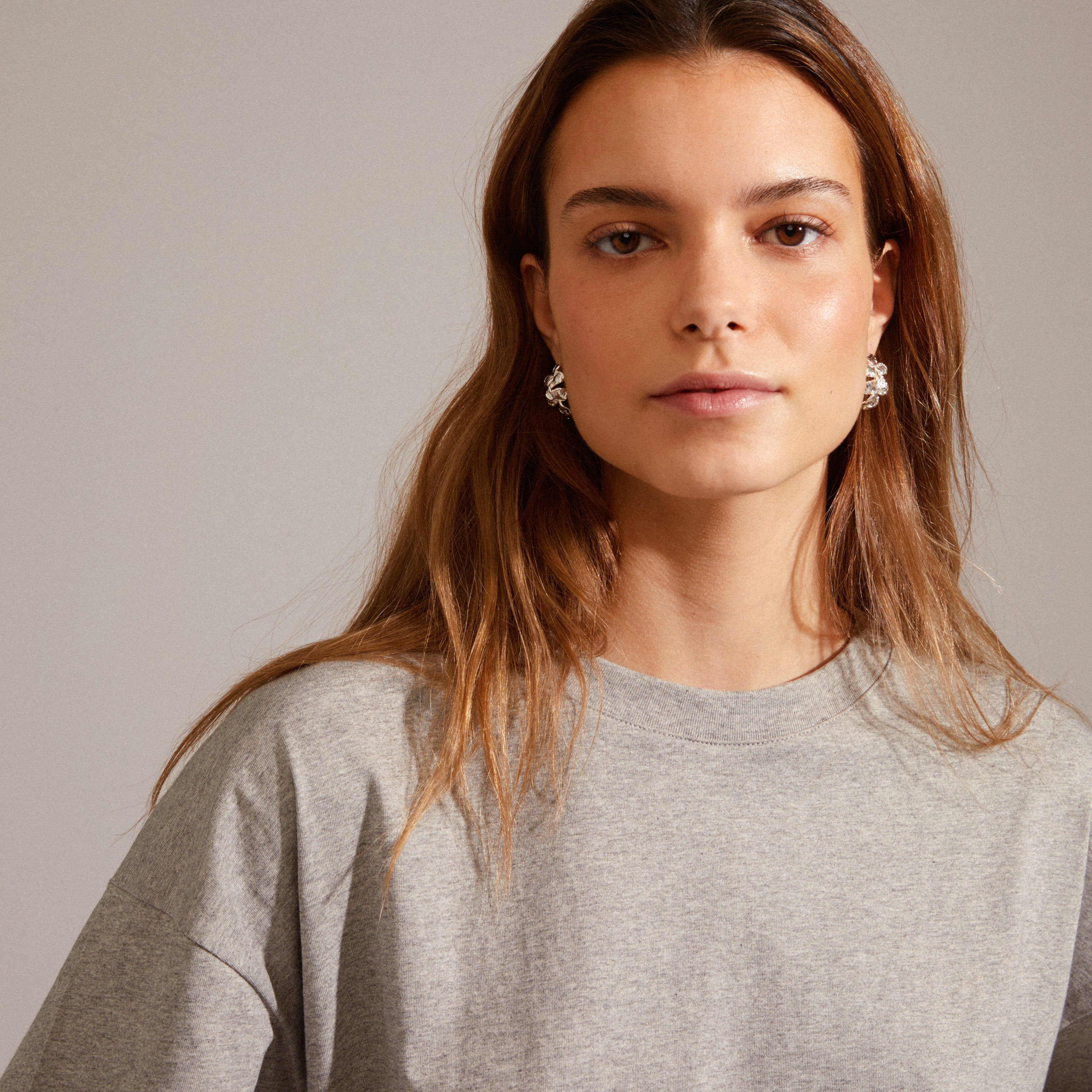 ECHO hoop earrings, silver-plated, worn by woman with long hair; features iconic flower design from Pilgrim, adding flair to a basic look.
