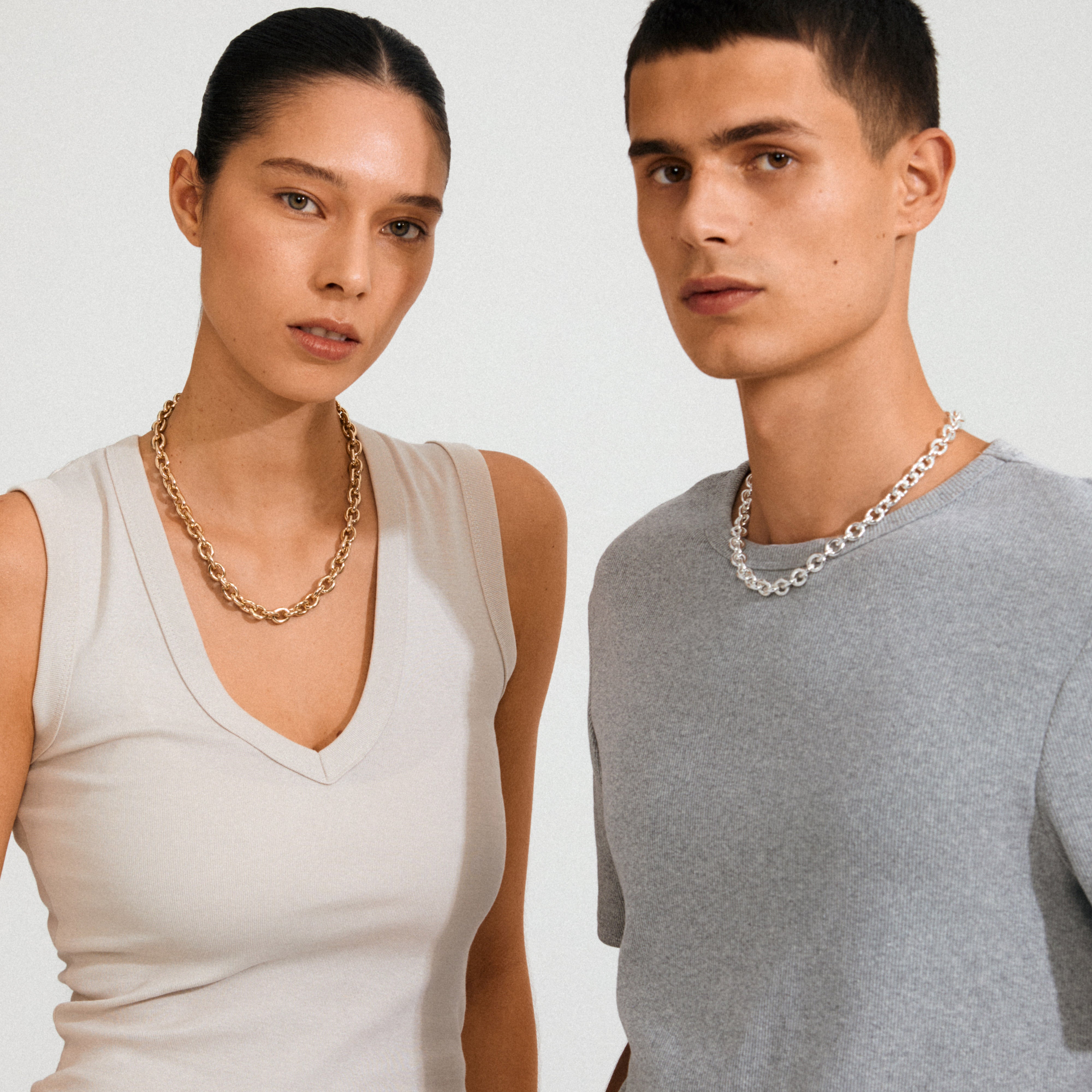 Two individuals showcase Pilgrim's PHASE necklace gold-plated, featuring a fluid cable chain and decorative clasp, embodying timeless design with an edgy, urban twist.