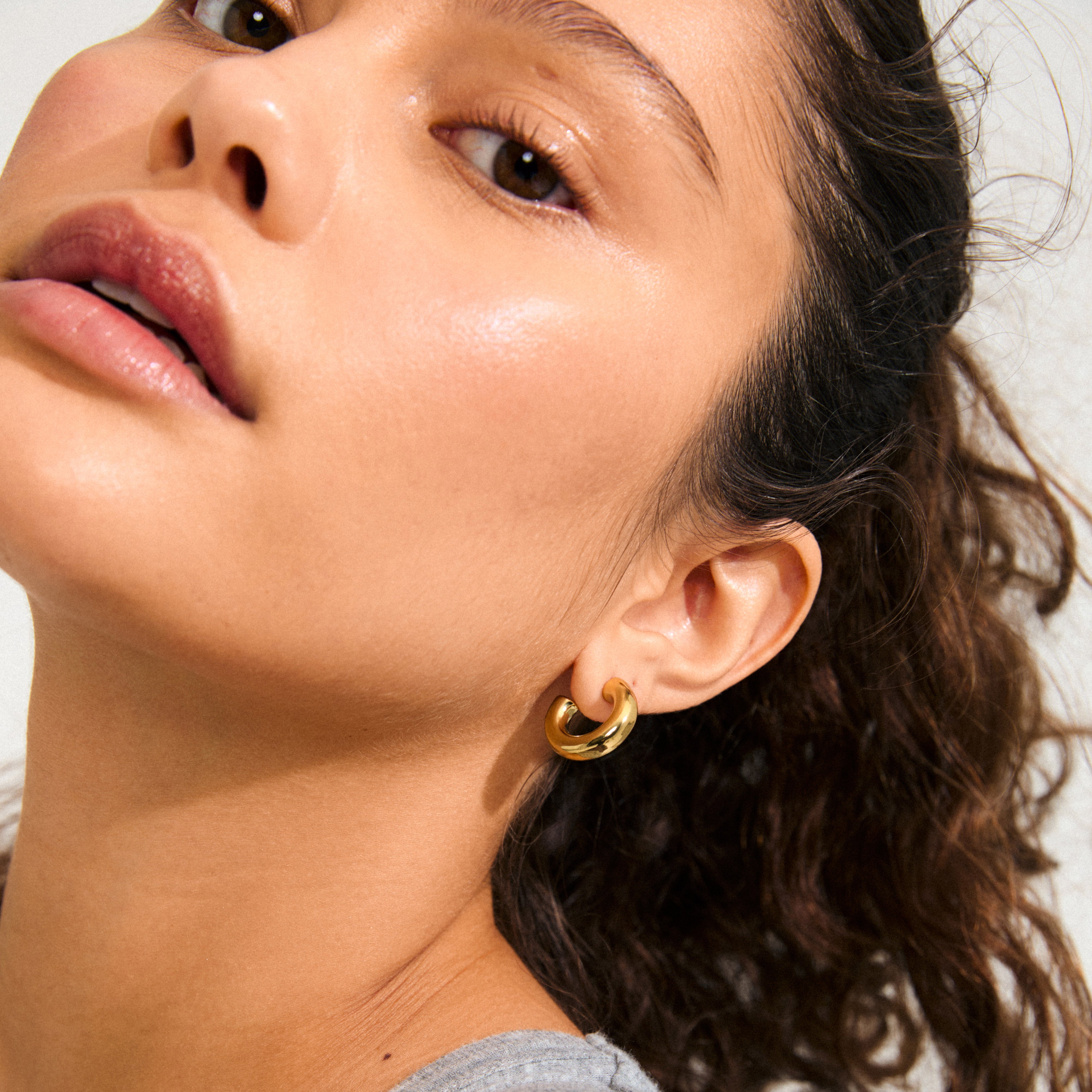Woman wearing Pilgrim's PHASE small gold-plated hoops, showcasing a chunky design for a refined, stylish look. Her hair is pulled back, revealing her earring.