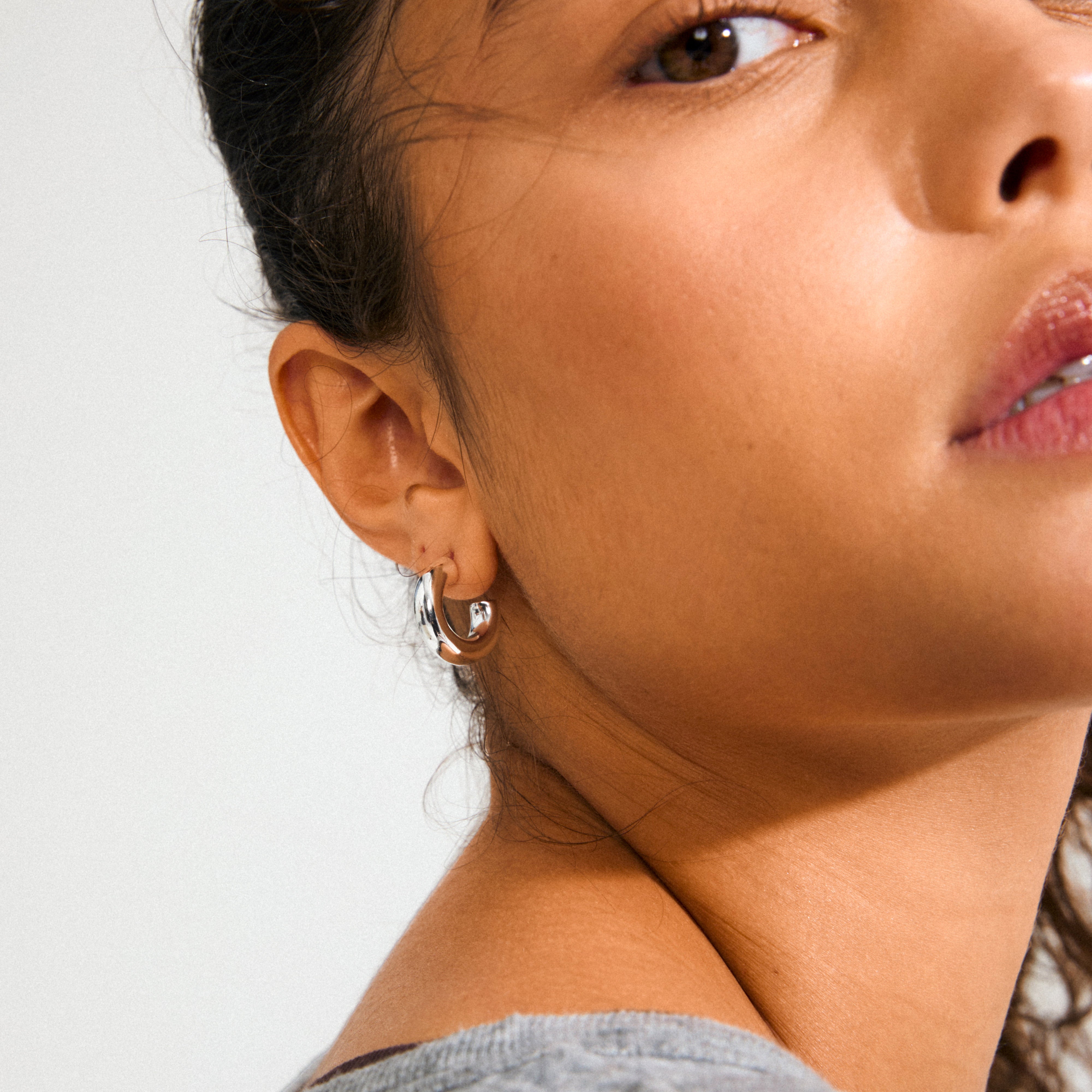 Close-up of a person wearing PHASE small silver-plated hoops from Pilgrim, highlighting their chunky silhouette and glossy finish against warm-toned skin.