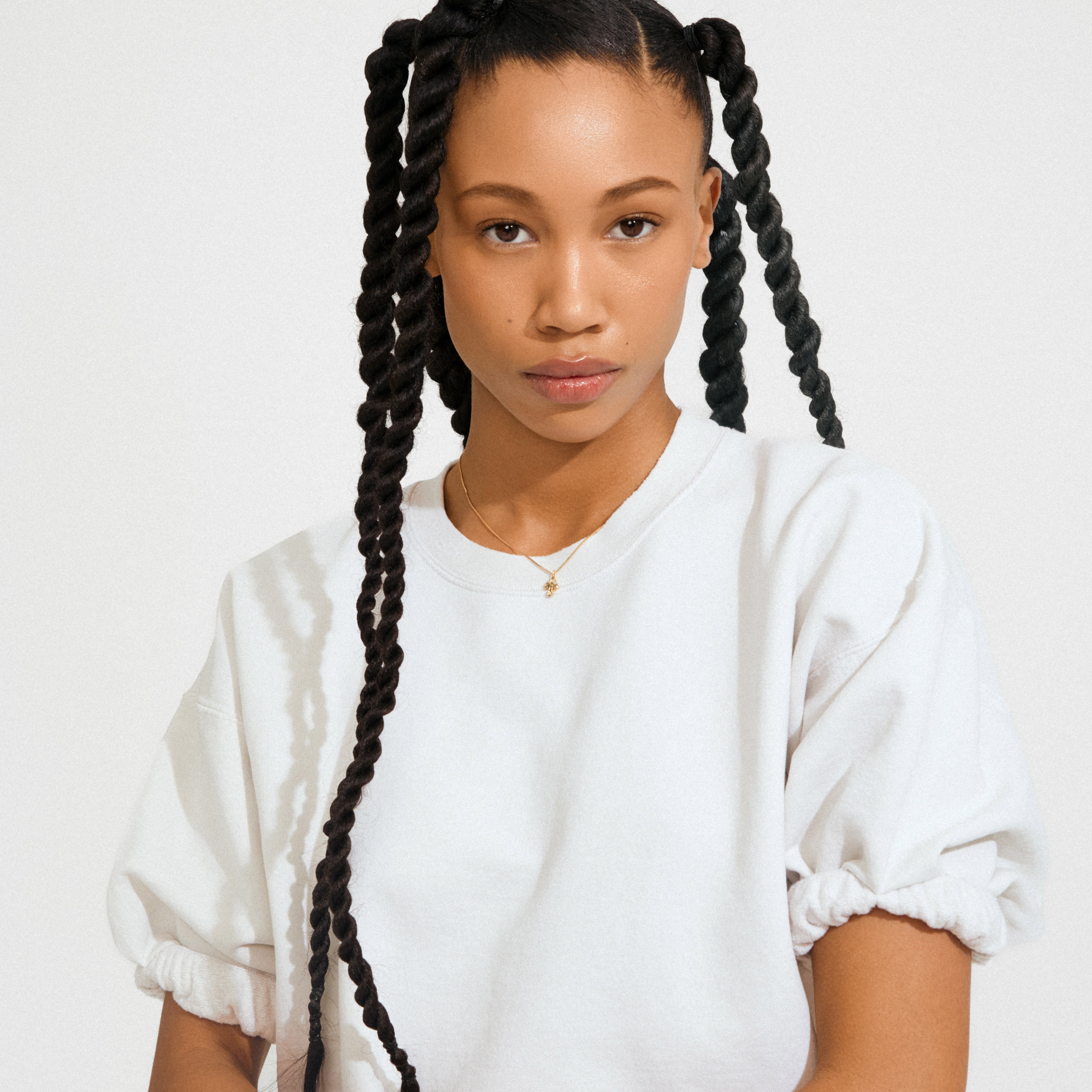 Young woman wearing the DAGMAR mini pendant necklace gold-plated, featuring a mini Dagmar Cross on a delicate chain, styled against a plain background.