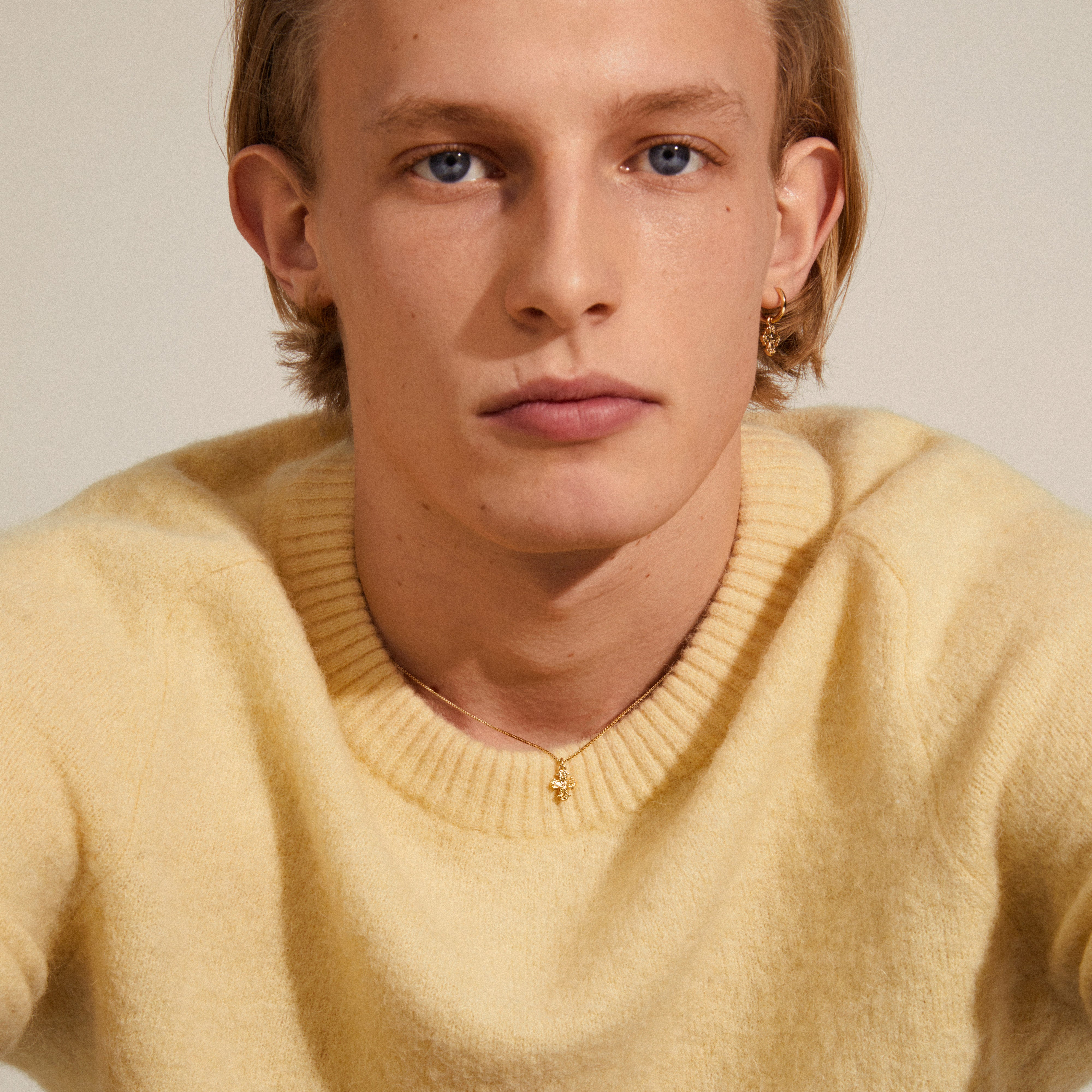 DAGMAR mini pendant necklace gold-plated on a man in a yellow sweater, showcasing the fine box chain and mini Dagmar Cross pendant.