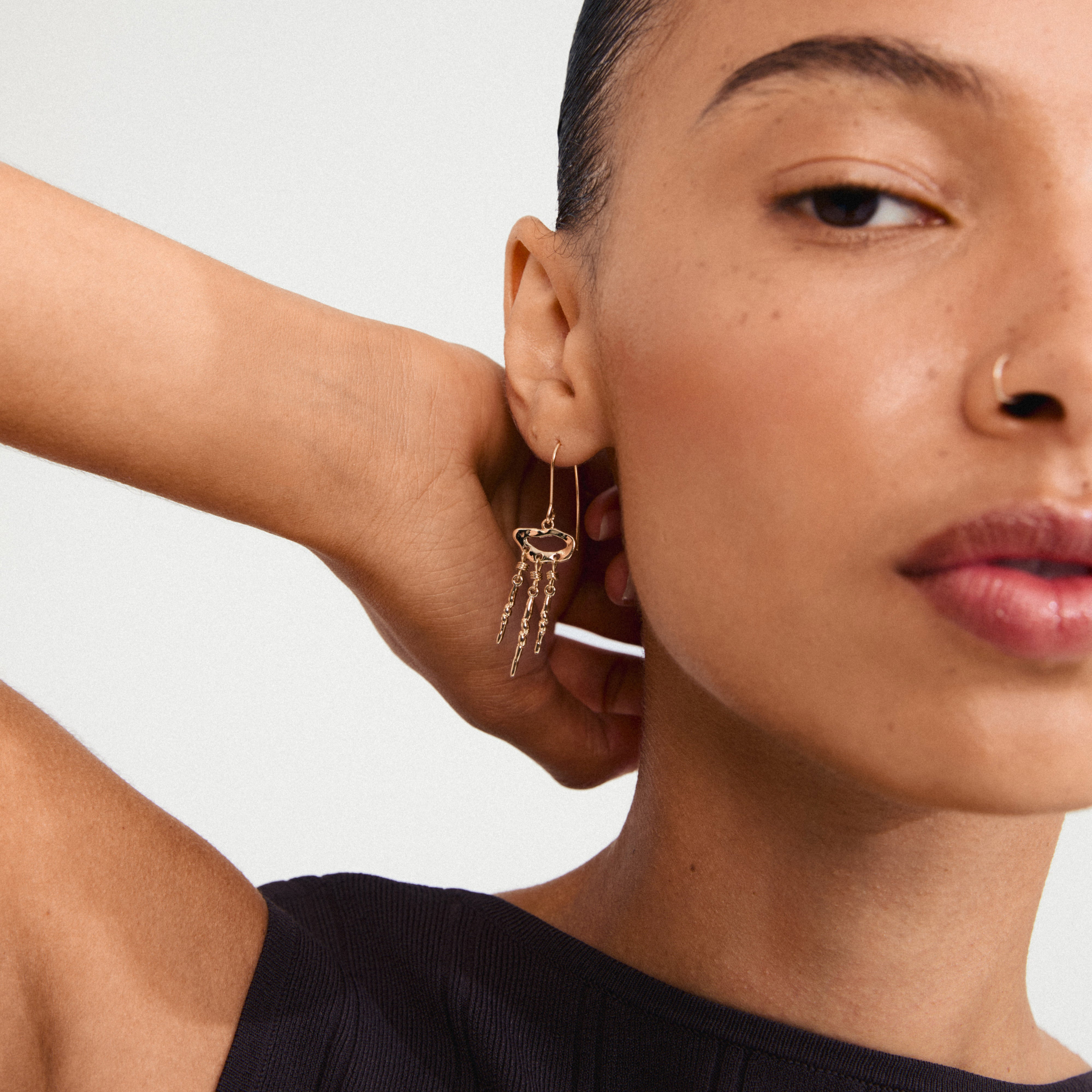 Close-up of a woman's ear wearing Pilgrim's BREEZE gold-plated earrings, showcasing their lively, fluid design inspired by dream catchers.