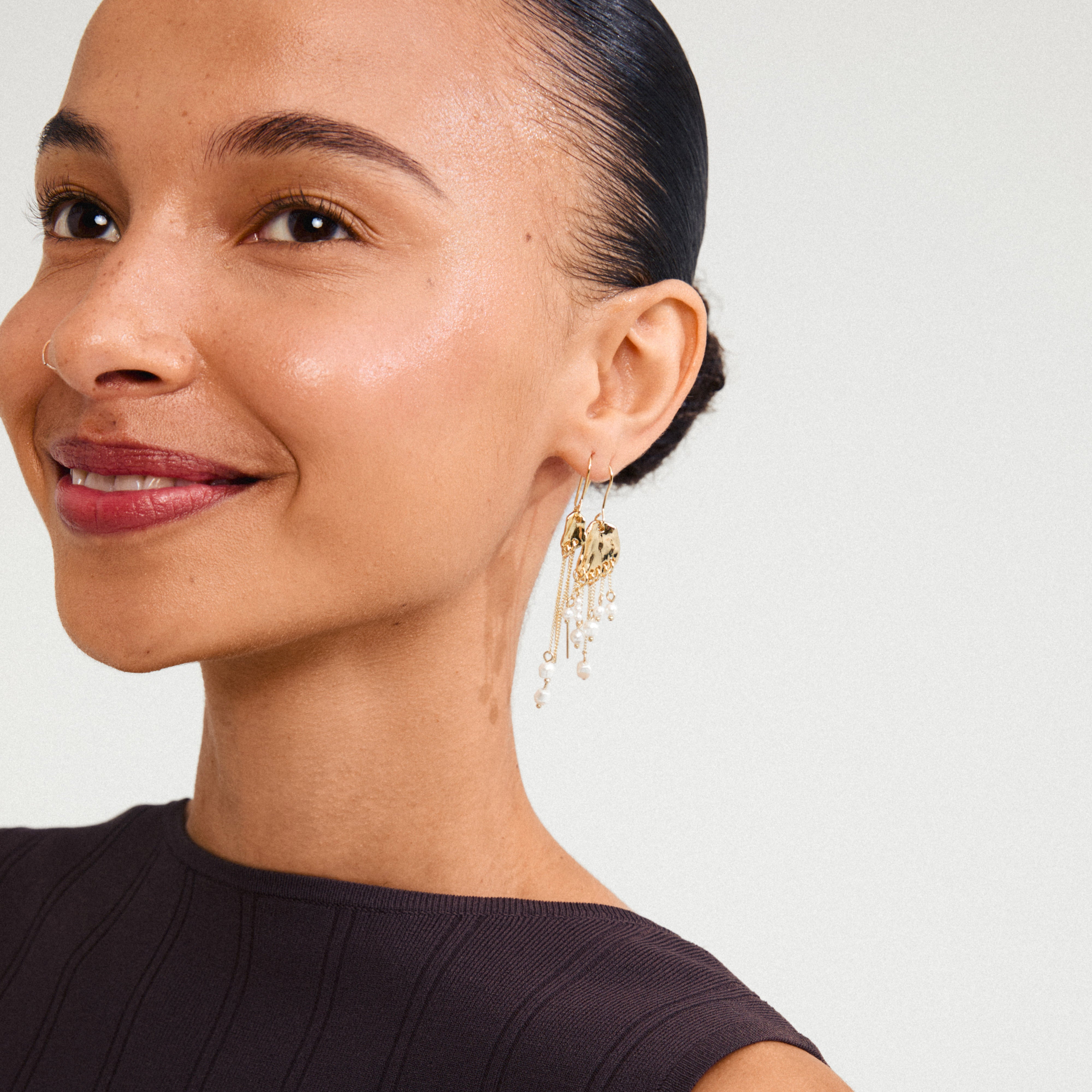 Close-up of a woman wearing BREEZE chain earrings, featuring asymmetric gold-plated chains with freshwater pearls, capturing a bohemian-chic look.