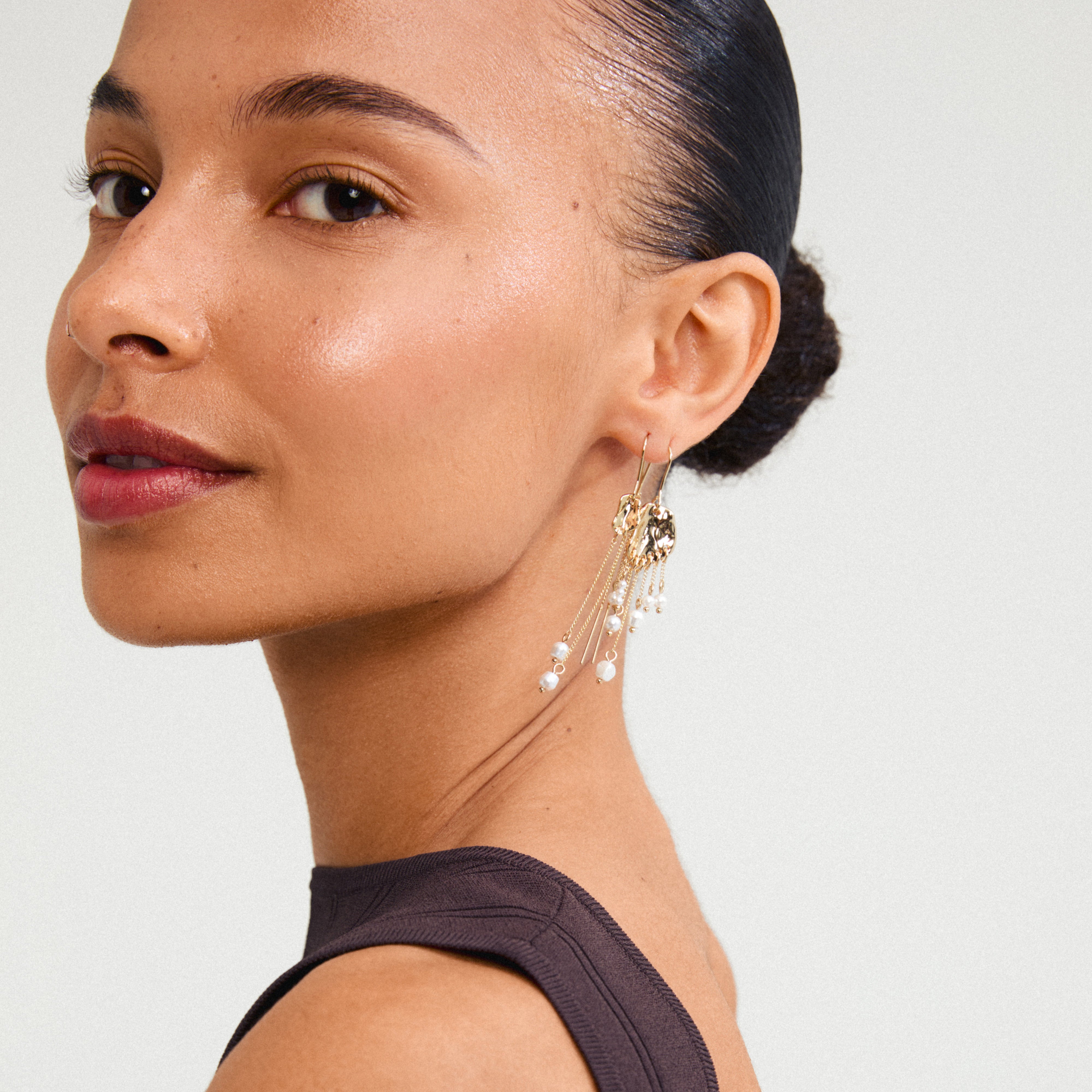 BREEZE chain earrings gold-plated with asymmetric chains and pearls, worn by a woman with a ponytail and earrings, capturing a bohemian-chic look.