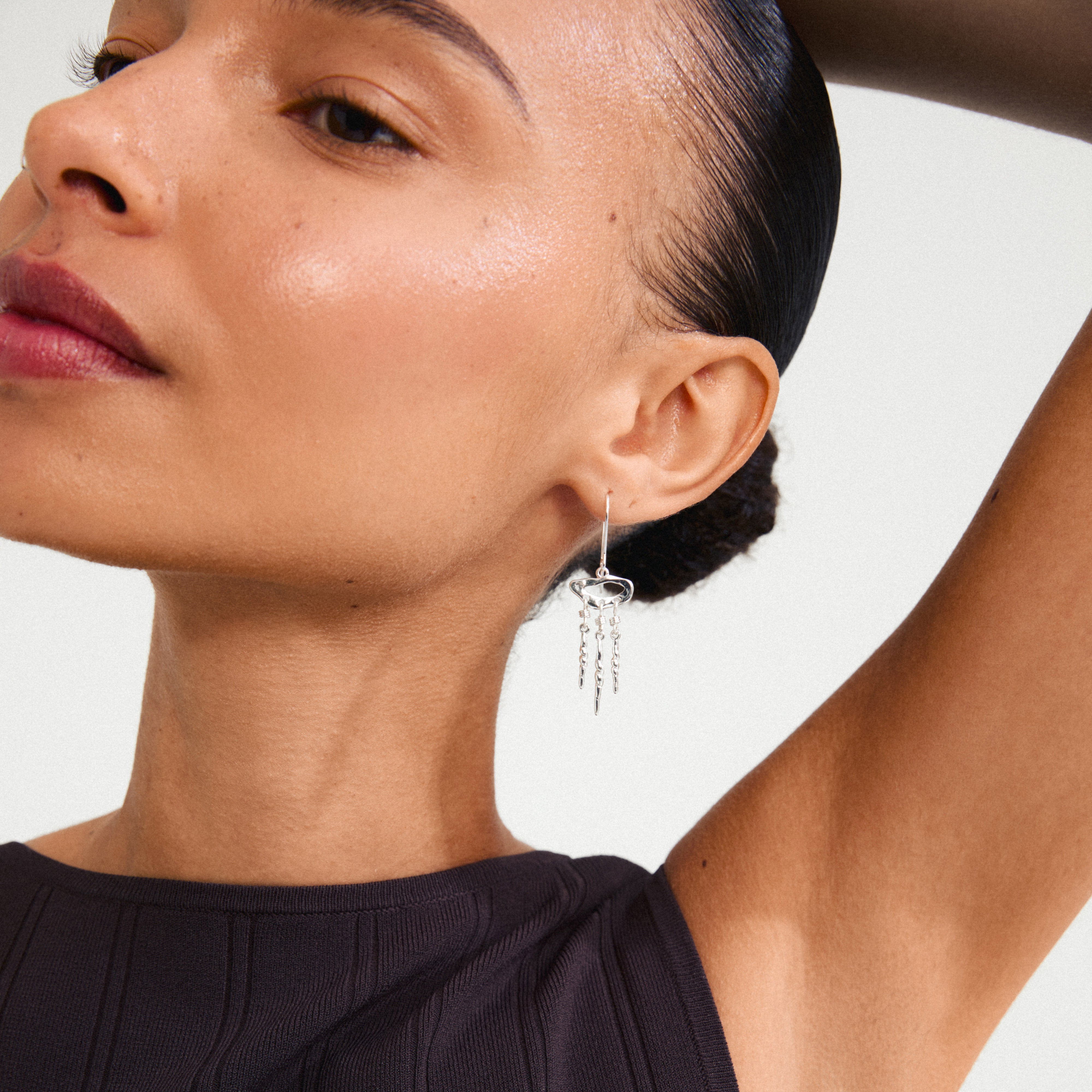 Silver-plated BREEZE earrings by Pilgrim, inspired by dream catchers, visible on a woman's ear, showcasing a lively, fluid design with a shiny finish.
