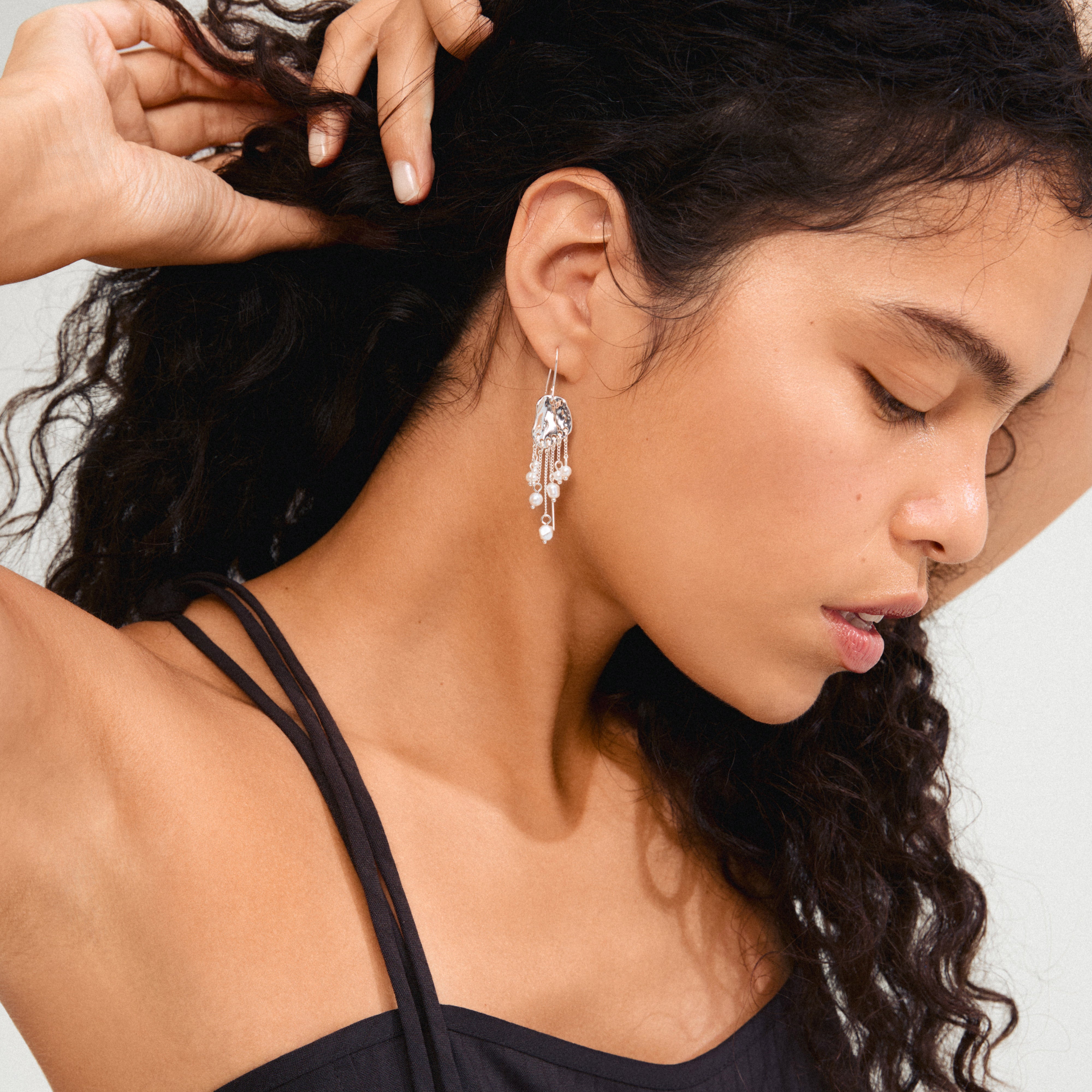 Close-up of a woman wearing BREEZE chain earrings, featuring asymmetrical silver-plated chains with freshwater pearls, capturing a dreamy, boho-chic style.