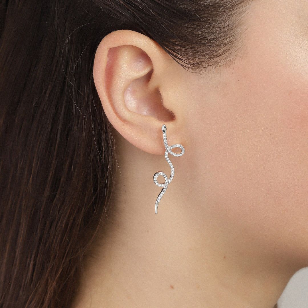 Close-up of a woman's ear adorned with EBBA crystal snake silver-plated earrings, showcasing the intricate, mythologically inspired design with sparkling crystals.