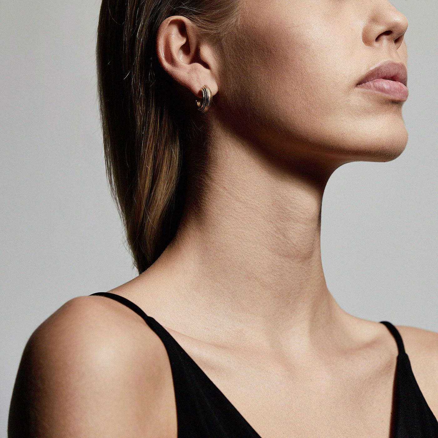 MACIE gold-plated hoop earrings showcased on a woman in a black dress, highlighting their glamorous and bold design.