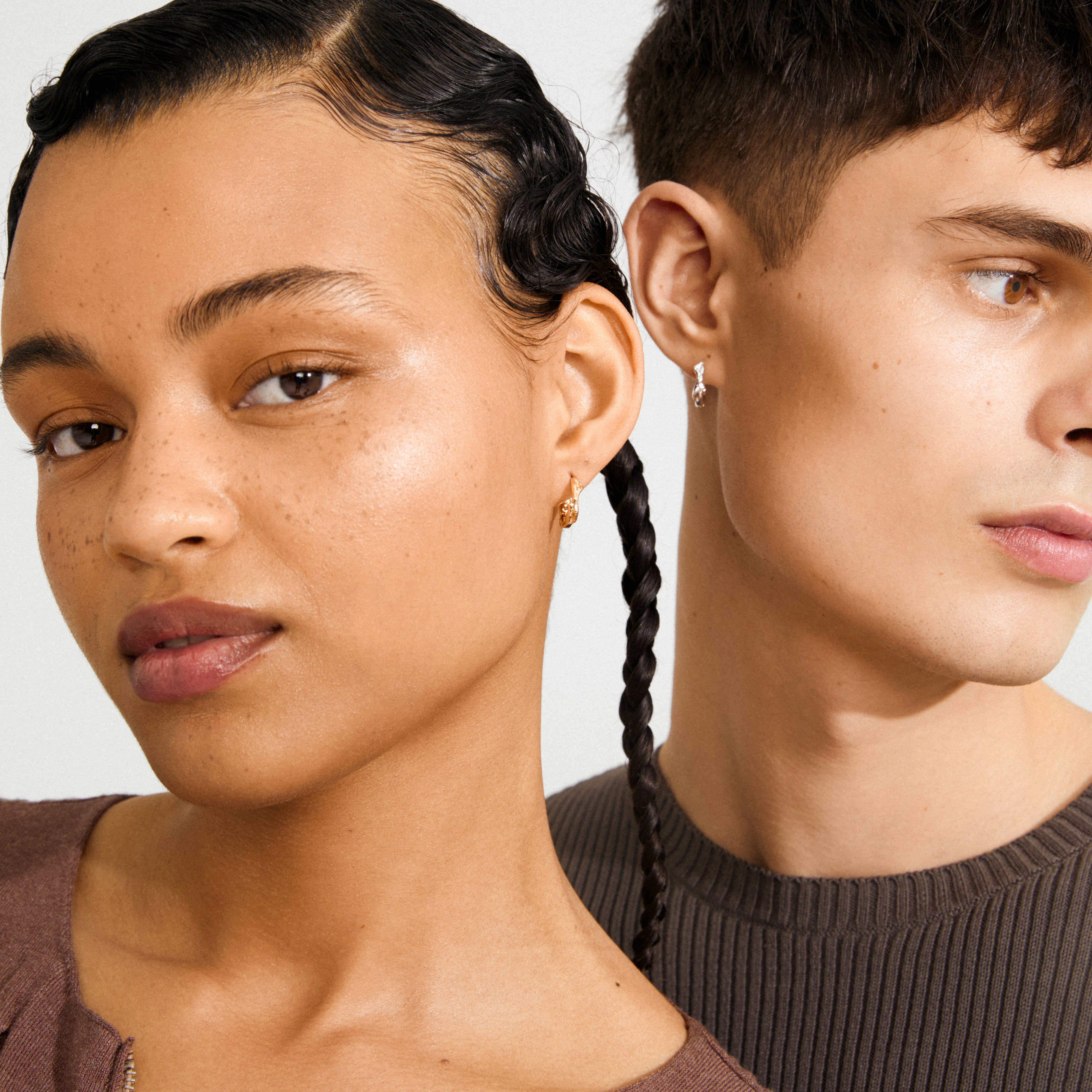 Models showcasing ZION small huggie hoop earrings, silver-plated—one in a gold charm, the other a twisted silver design, highlighting creative, stylish accessories.