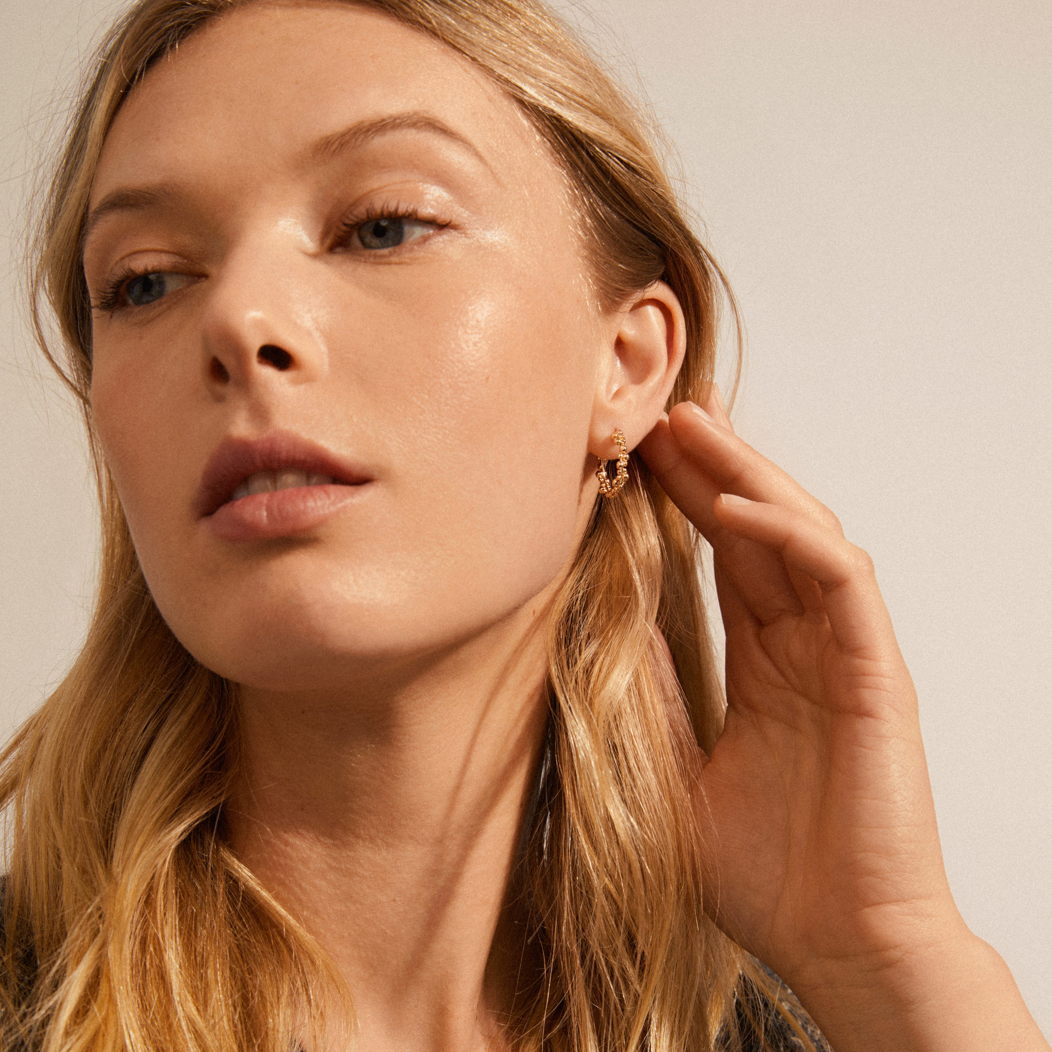 Woman with blonde hair wearing gold-plated SOLIDARITY medium bubbles hoop earrings, showcasing their asymmetric bubble shapes and stylish, dynamic silhouette.