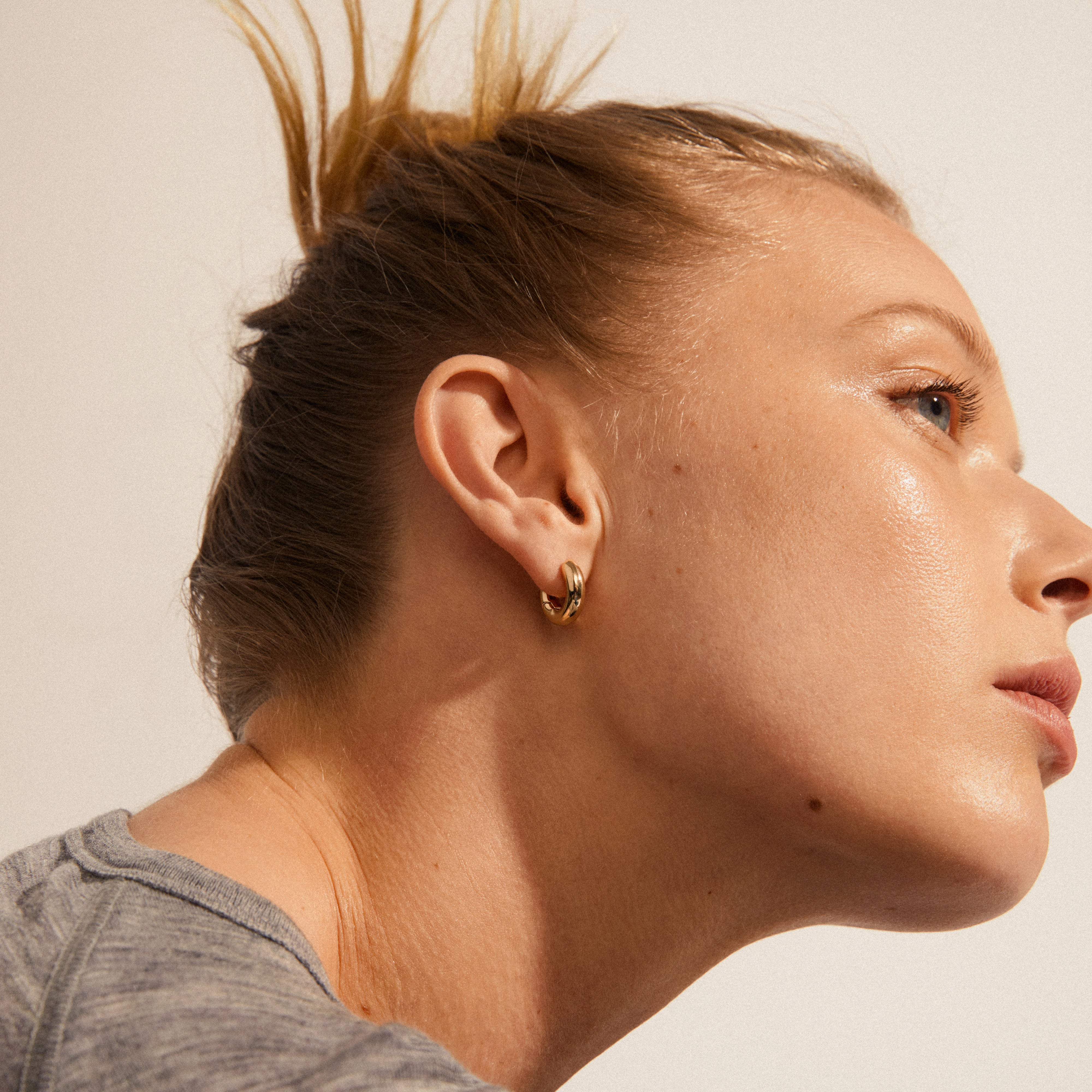 Close-up of a woman wearing Pilgrim's AICA chunky huggie hoop earrings, gold-plated, highlighting their minimalist, shiny design and comfortable click lock.