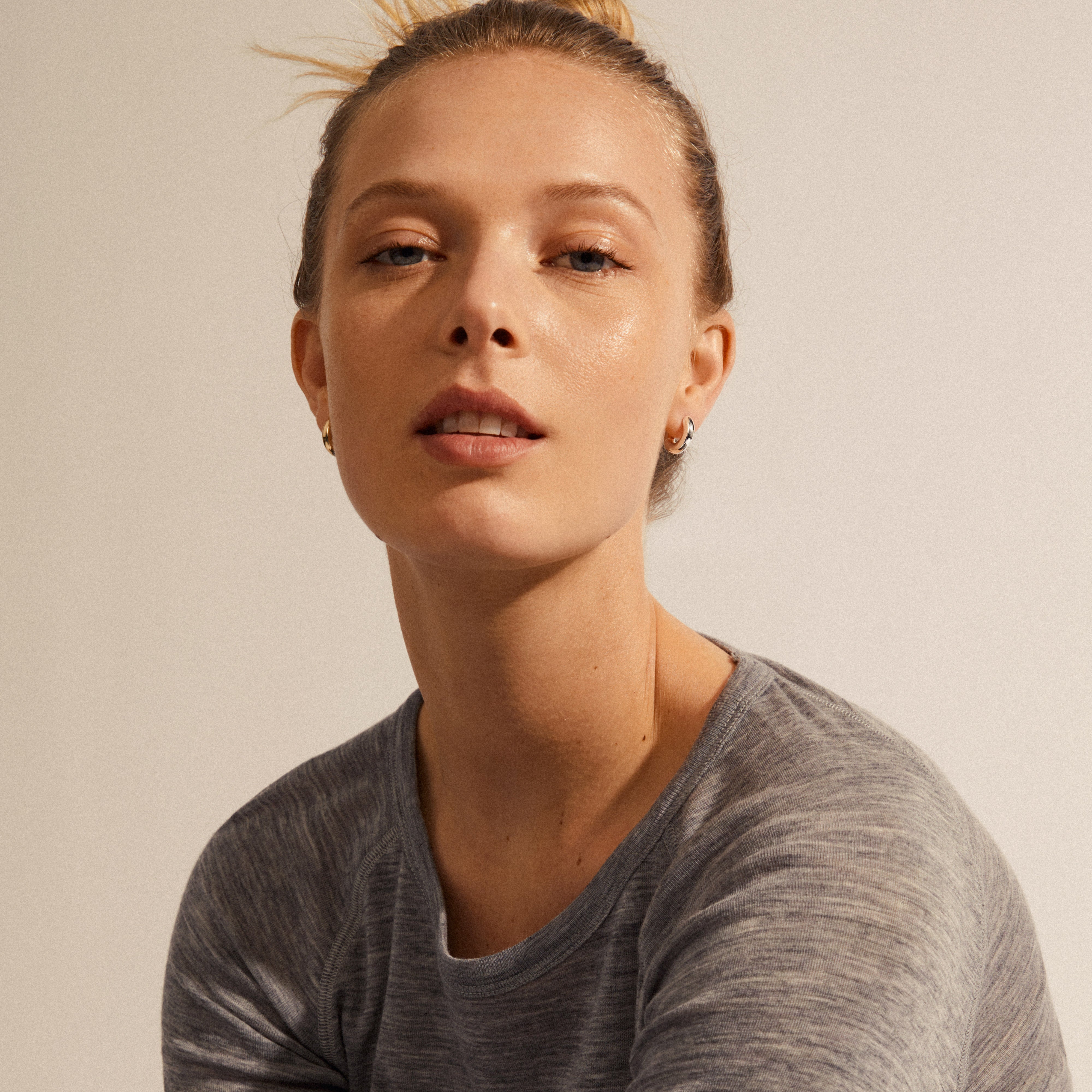 A woman wearing AICA chunky huggie hoop earrings, silver-plated, showcasing their minimalist, shiny design, ideal for everyday wear.