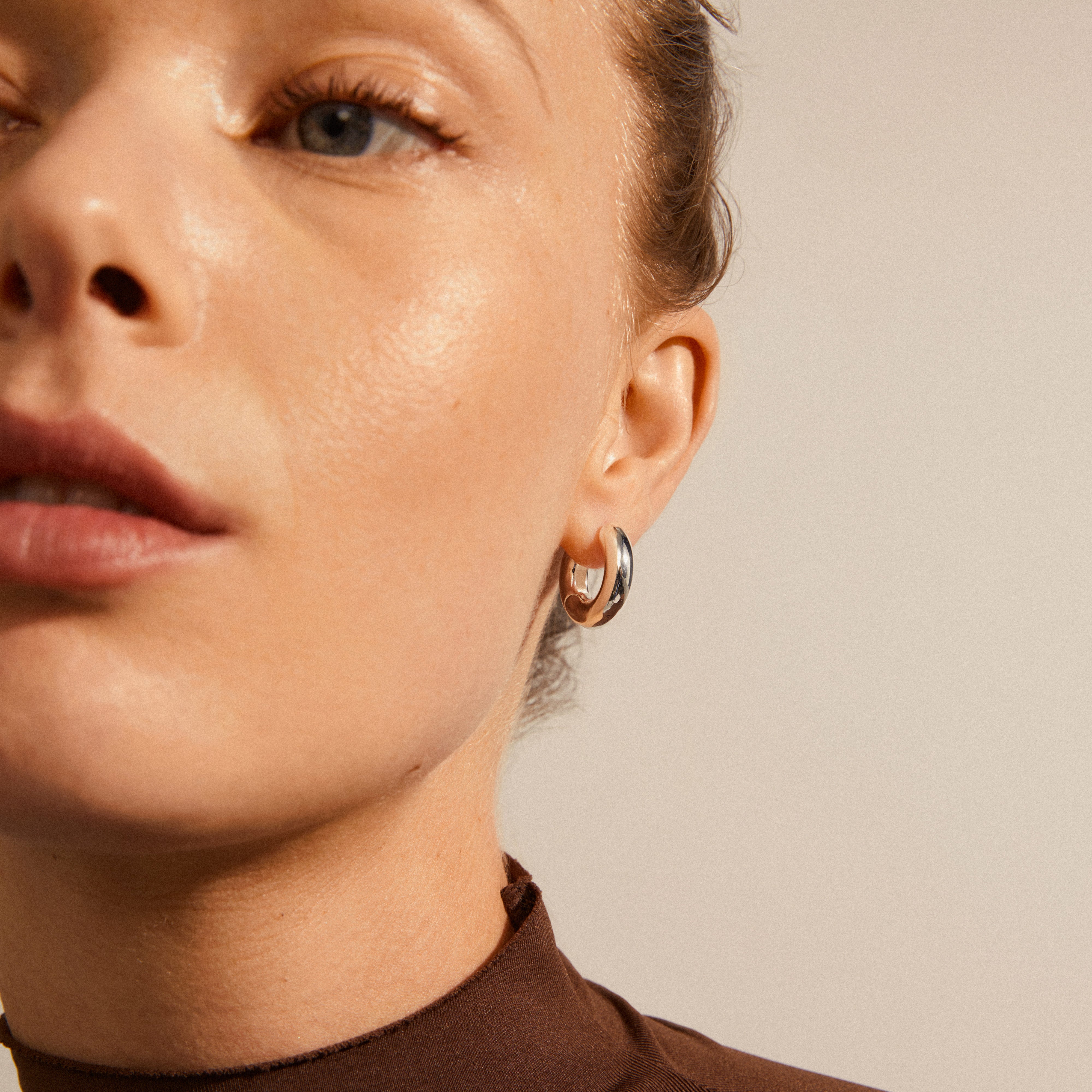 Close-up of a woman's face showcasing AICA chunky hoop earrings, silver-plated with a click lock, highlighting their timeless, trendy design for everyday wear.