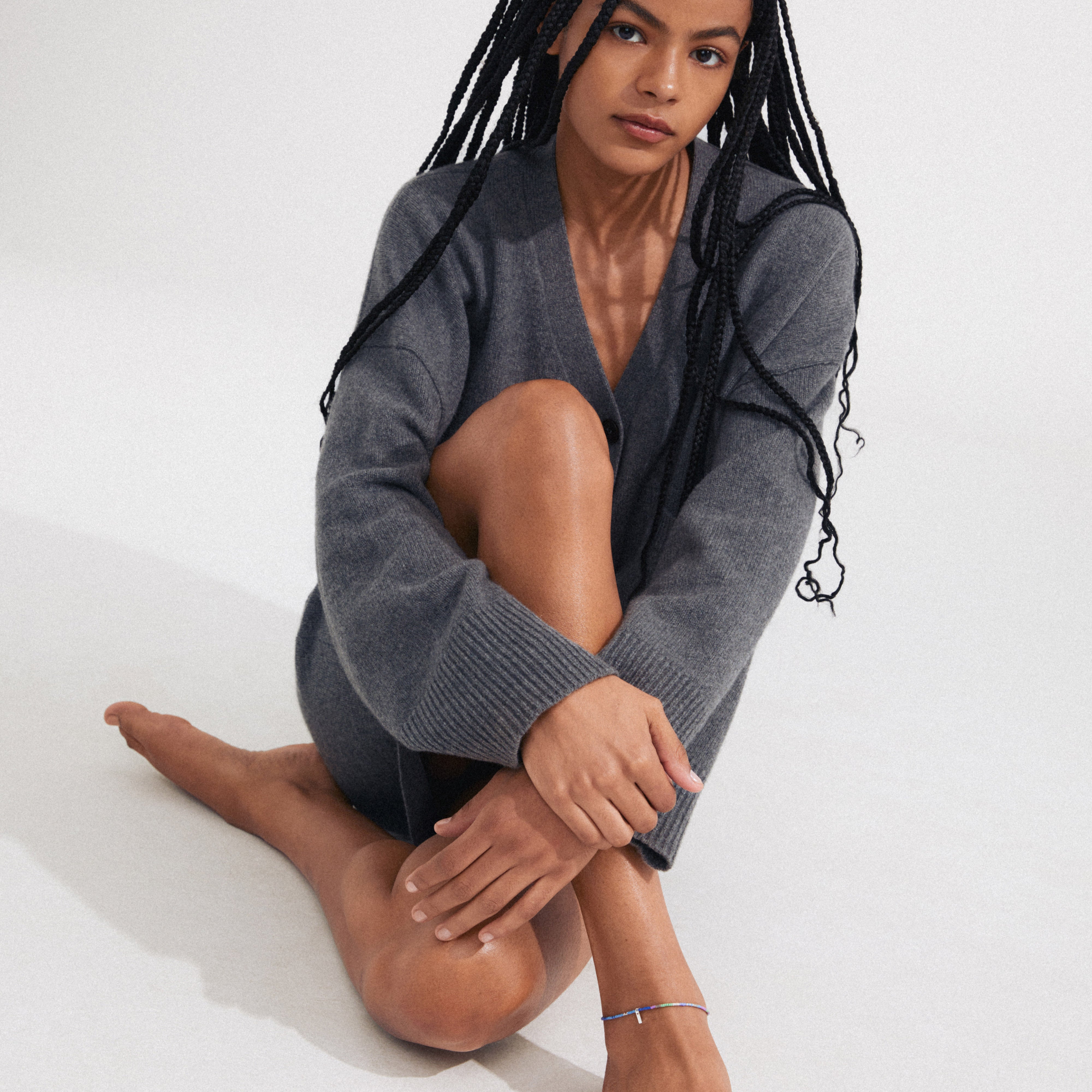 Woman with braided hair wearing the ALISON ankle chain, featuring silver-plated glass beads, sitting on the floor, showcasing the accessory's stylish boho charm.